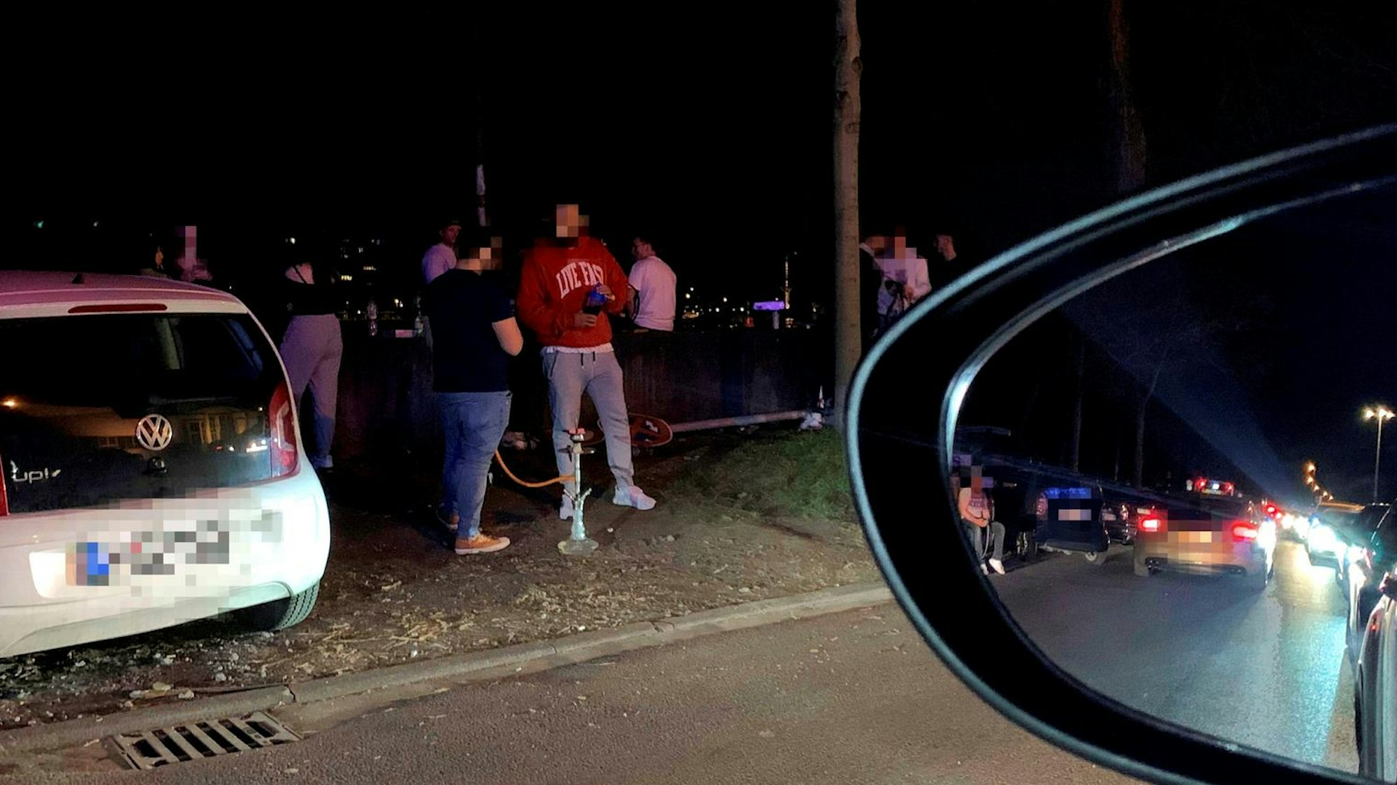 Junge Männer stehen auf der Alfred-Schütte-Allee zwischen geparkten Autos und rauchen Wasserpfeife.