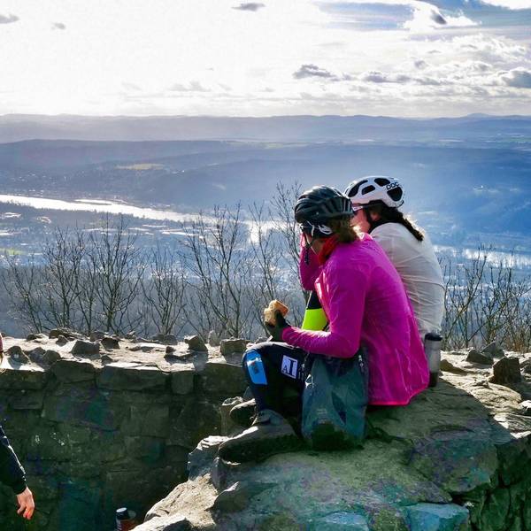 Drei Frauen machen auf dem Gipfel eines Berges Pause und sitzen dabei auf einer Steinmauer.