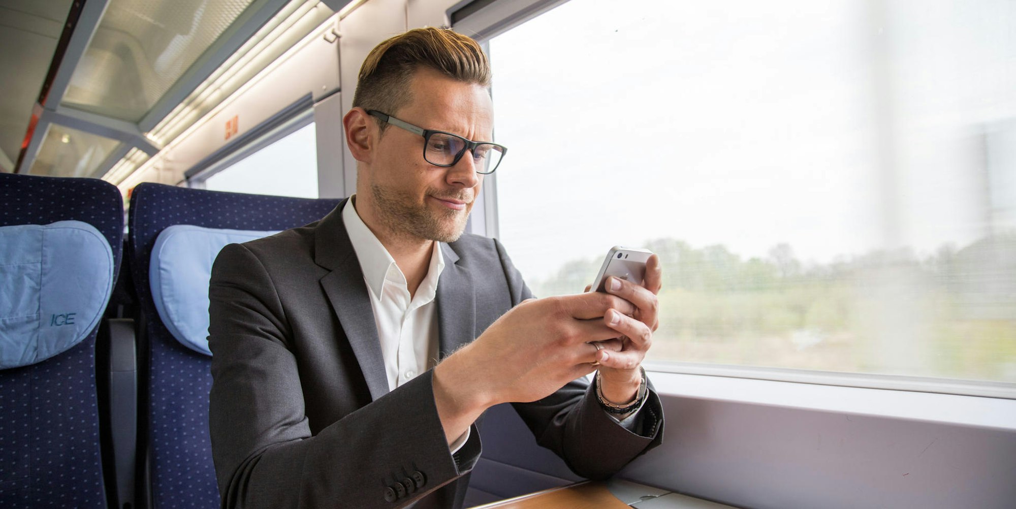 Mann sitzt mit Handy im ICE und sucht nach dem Handyempfang