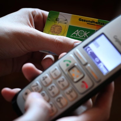 Hände halten ein Telefon und eine Krankenversichertenkarte