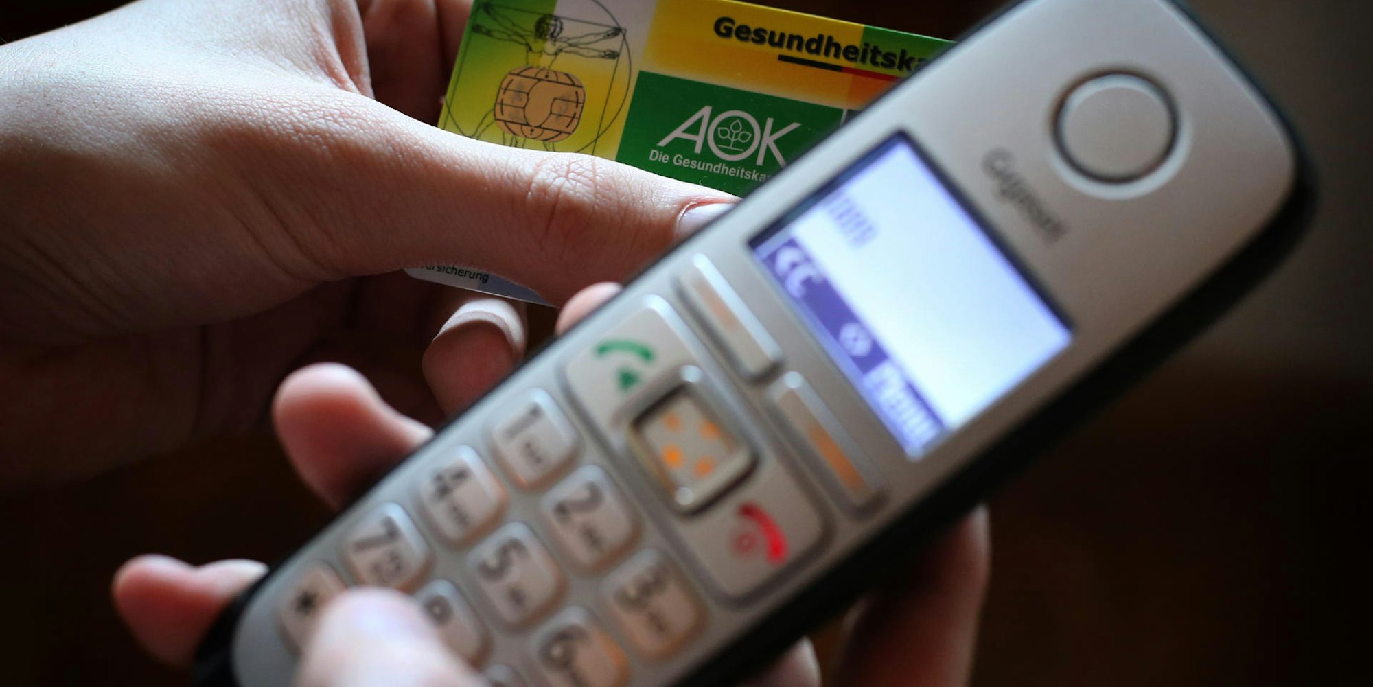 Hände halten ein Telefon und eine Krankenversichertenkarte