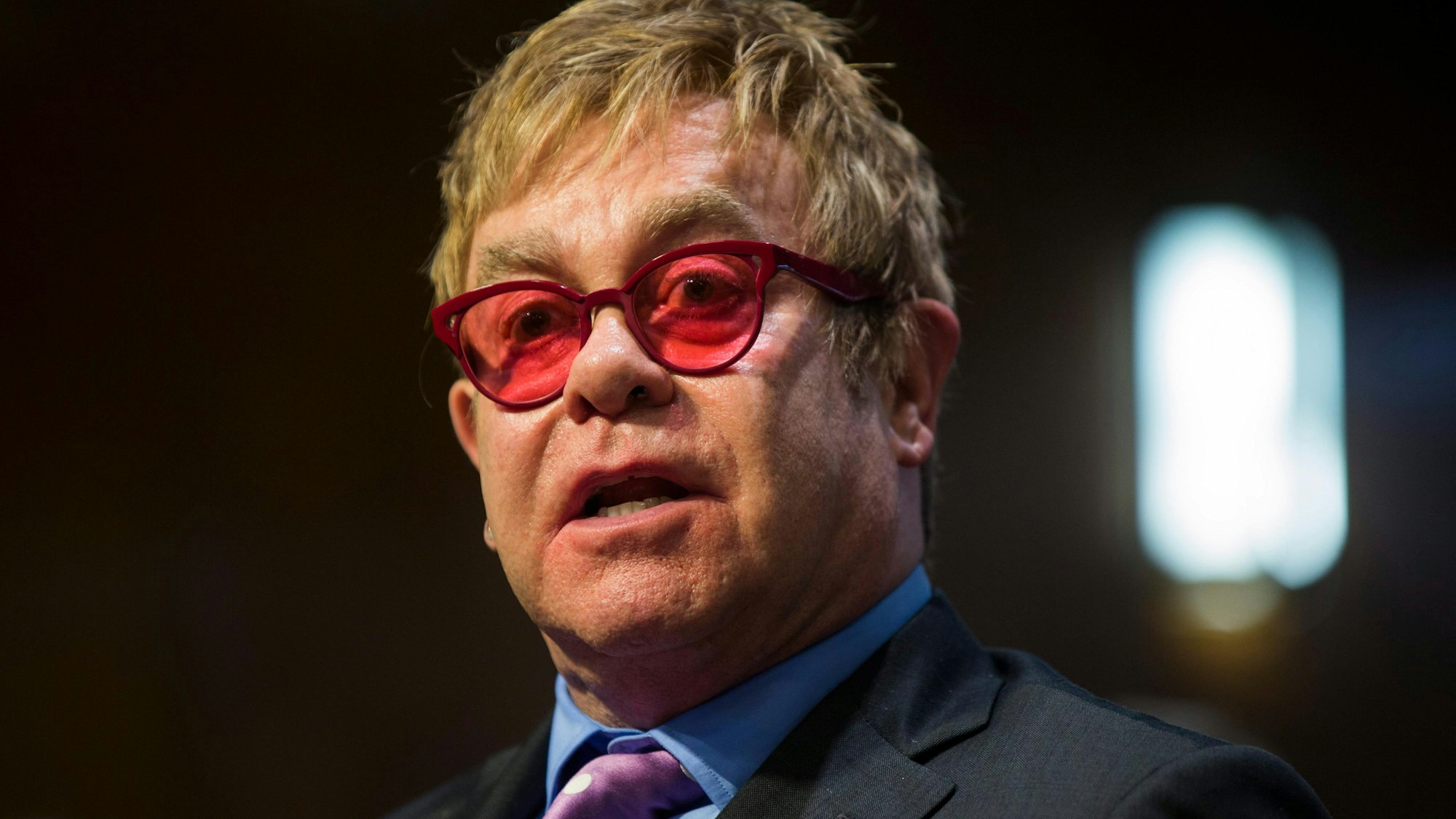 Elton John mit roter Brille bei einem öffentlichen Auftritt.