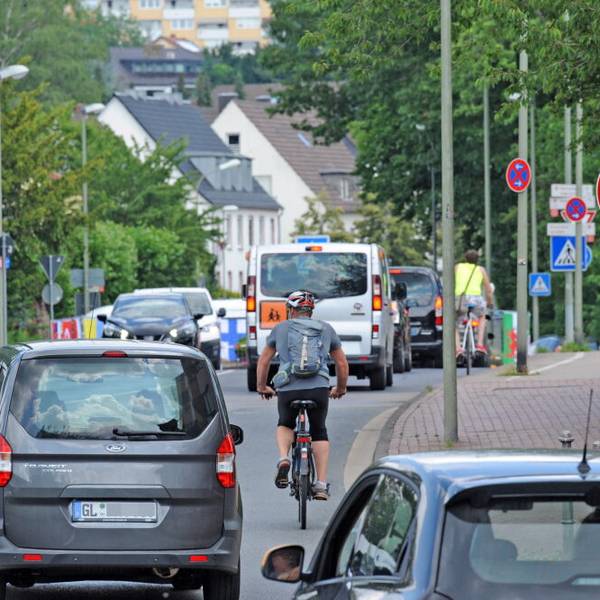 Autos, Kleinbus und Radfahrer auf einer Straße.