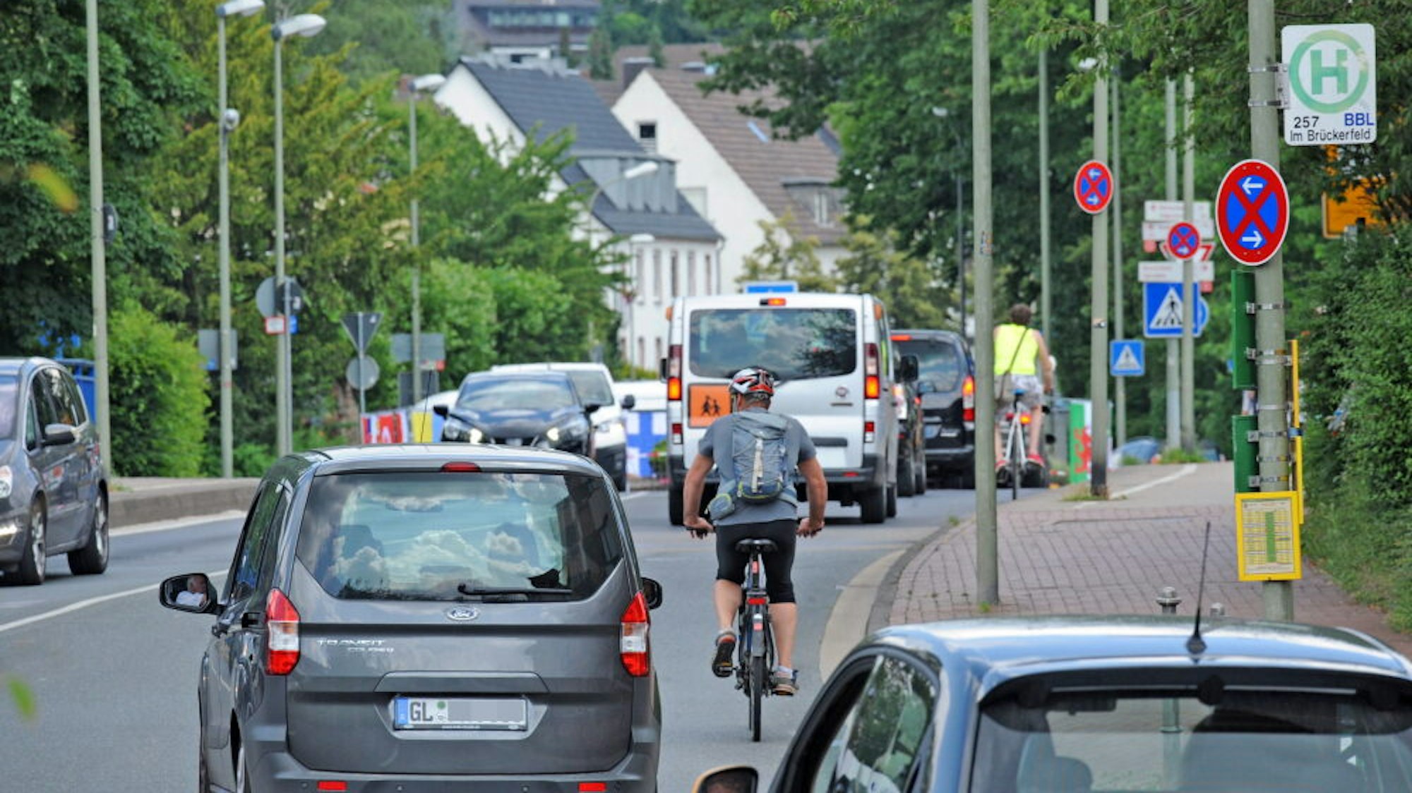 Autos, Kleinbus und Radfahrer auf einer Straße.