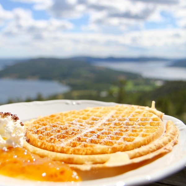 Waffel mit Sahne vor Landschaft und Gewässer im Hintergrund.