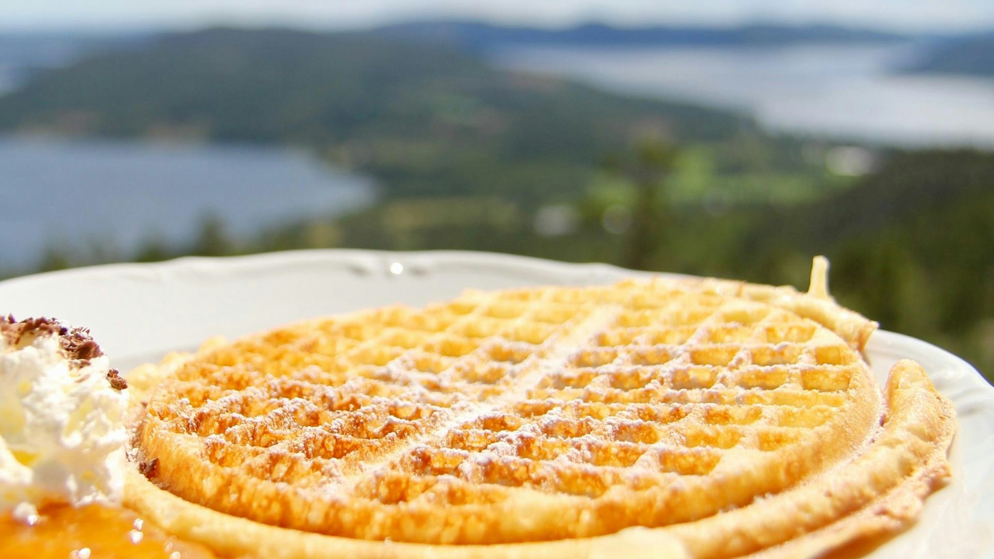 Waffel mit Sahne vor Landschaft und Gewässer im Hintergrund.