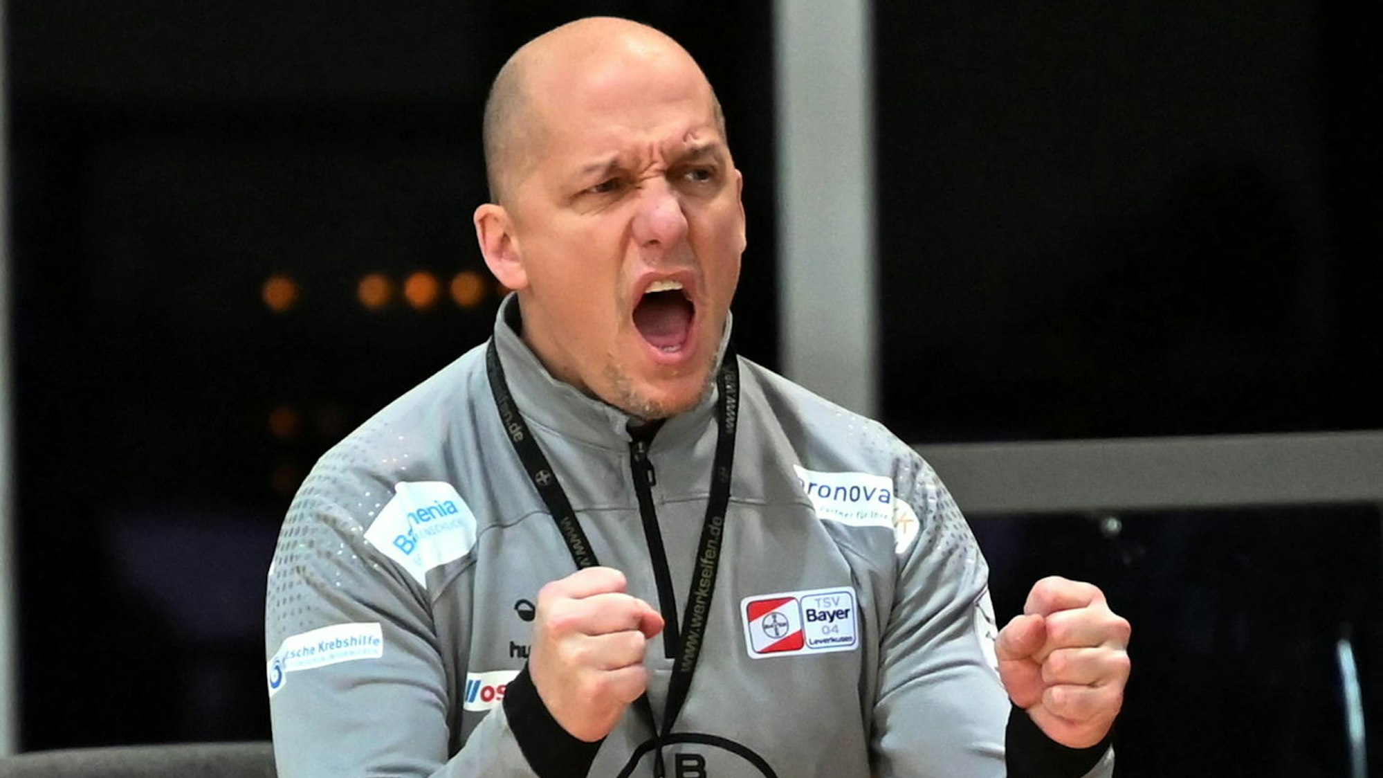 Ein Handballtrainer steht am Spielfeldrand und ballt die Fäuste zum Jubel.