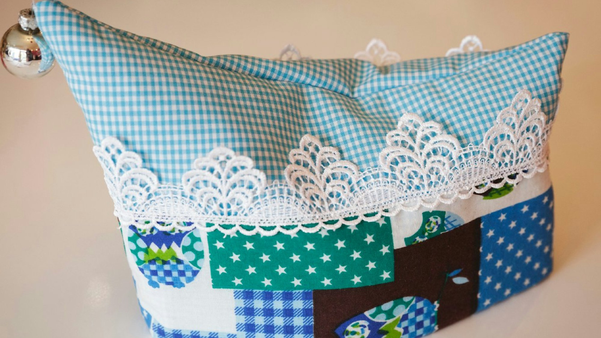 Blaugrüne Narrenkappe mit unterschiedlichen Mustern und Stoffen mit Spitzenbordüre.