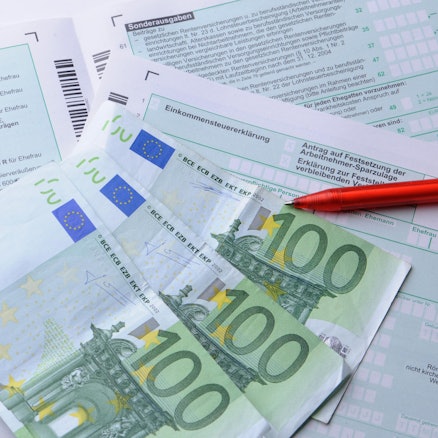 Geldscheine und ein Stift liegen auf einem Formular für die Steuererklärung.