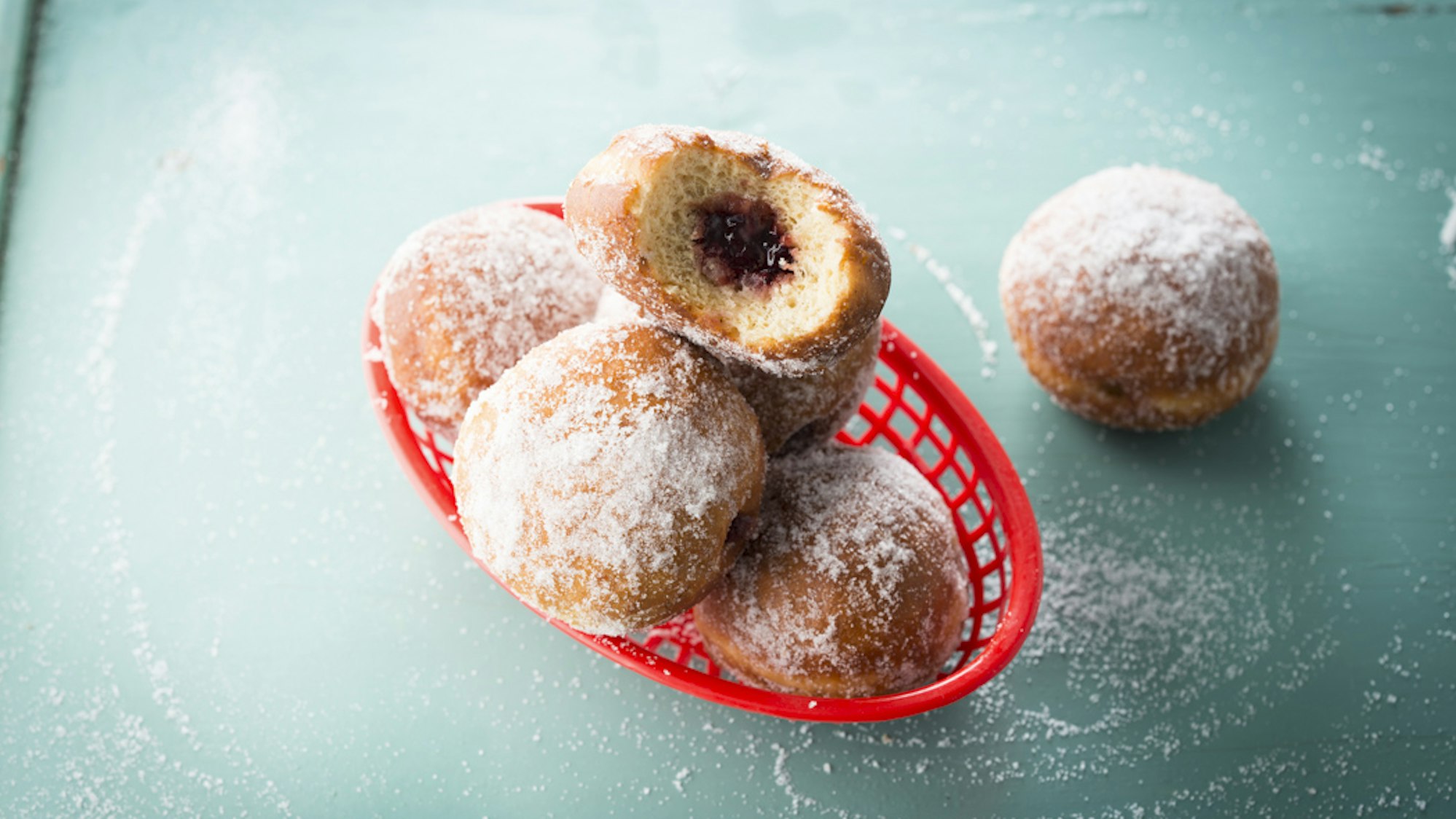 Berliner liegen auf einer Arbeitsplatte, bei einem sieht man die Erdbeerfüllung.