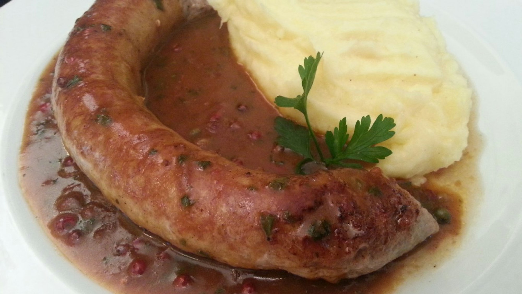 Bratwurst und Kartoffelbrei in brauner Soße auf einem Teller im Haus Scholzen in Köln.