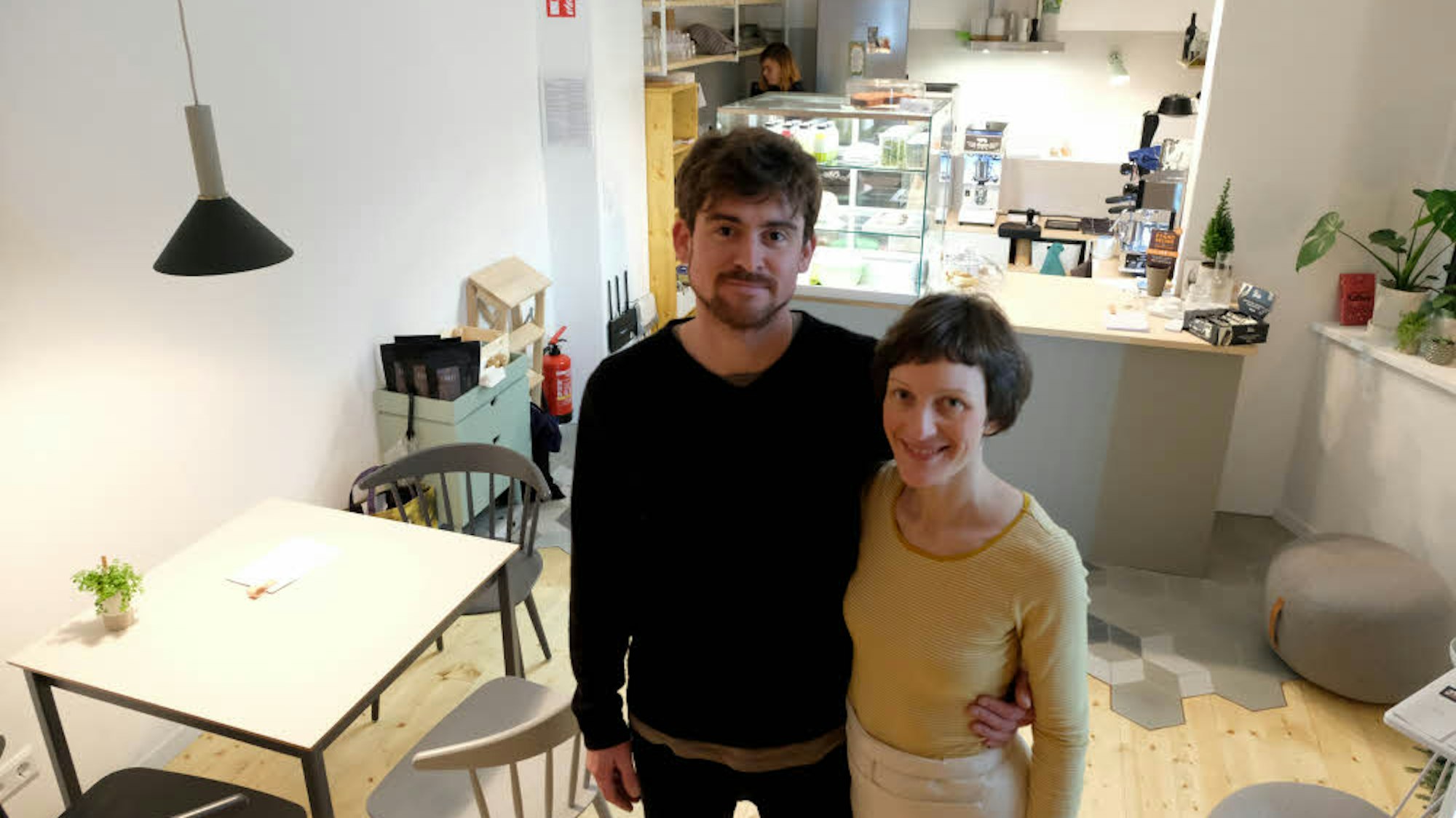 Die Inhaber des Café Südlicht in Köln stehen Arm in Arm in ihrem Laden.