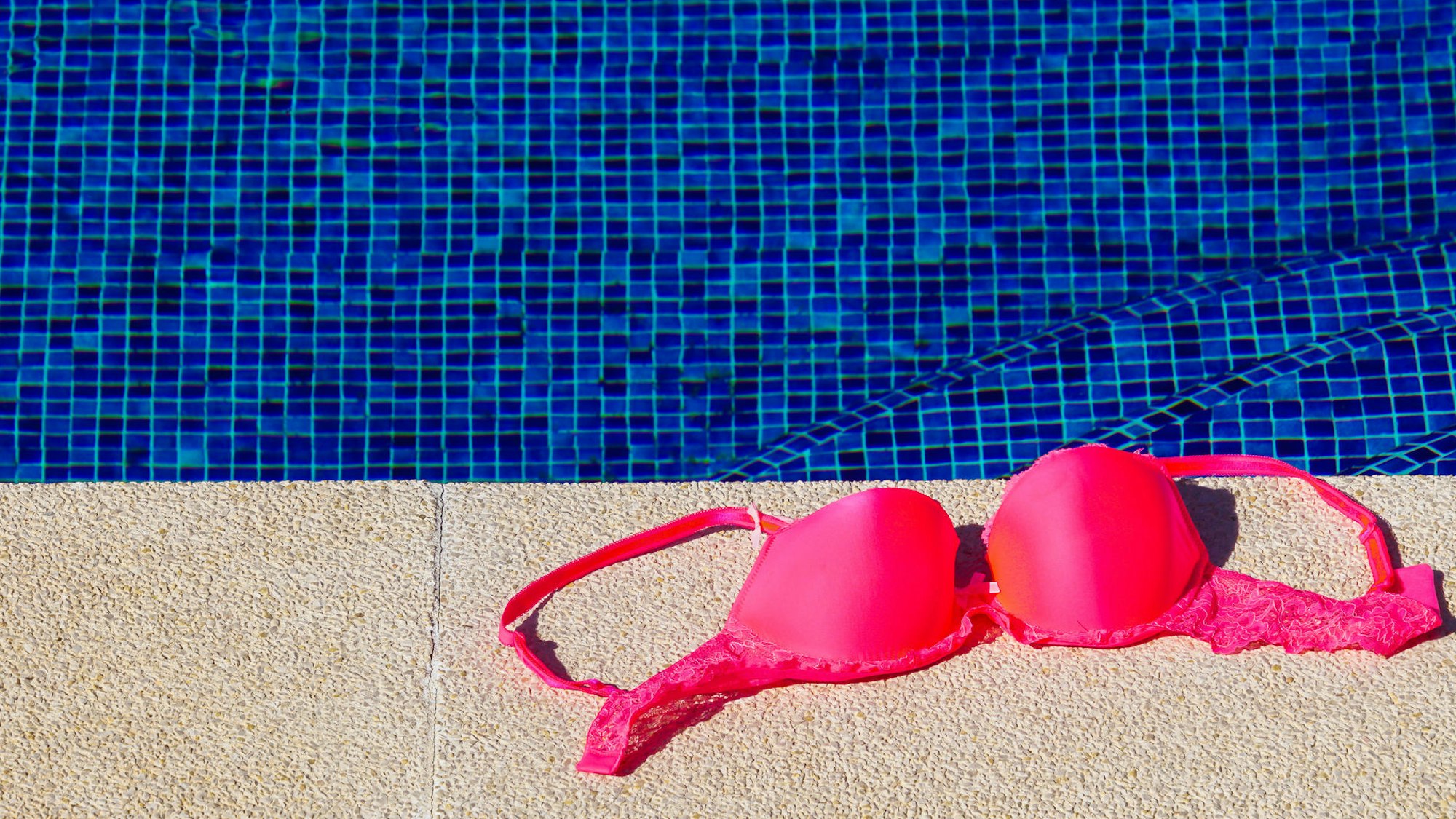 Ein Bikinioberteil liegt am Rand von einem Schwimmbecken.