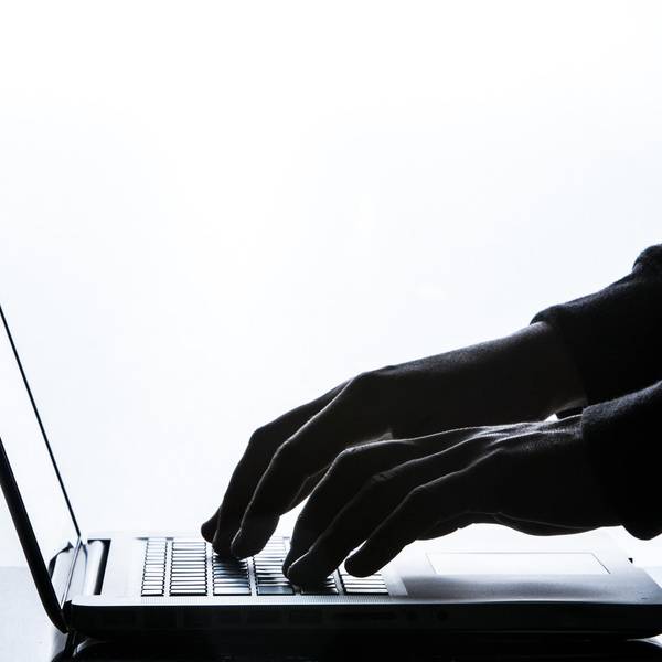 Hände in Handschuhen tippen auf der Tastatur eines Laptops.