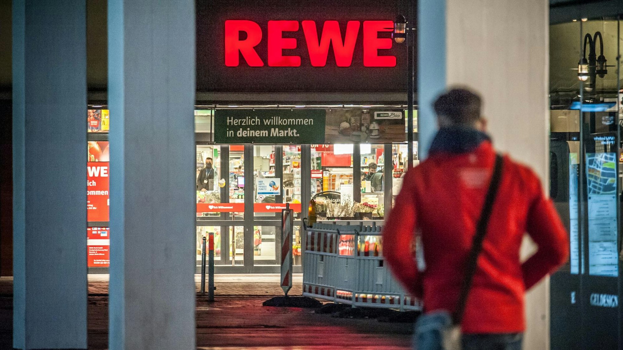 Eine Person geht auf einen Rewe Supermarkt zu.