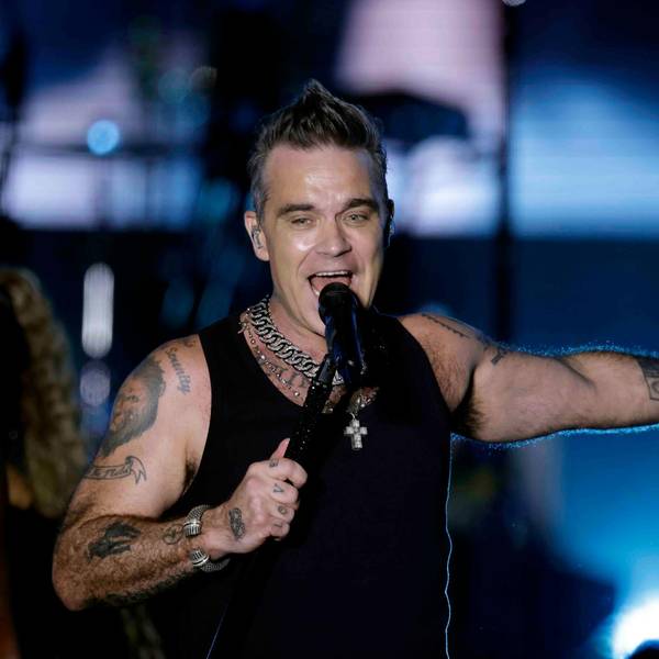 Der britische Sänger Robbie Williams am 30. August 2022 auf der Bühne im Bonner Hofgarten. Er singt ins Standmikrofon, trägt ein Muscle-Shirt und hat einen Arm ausgestreckt.