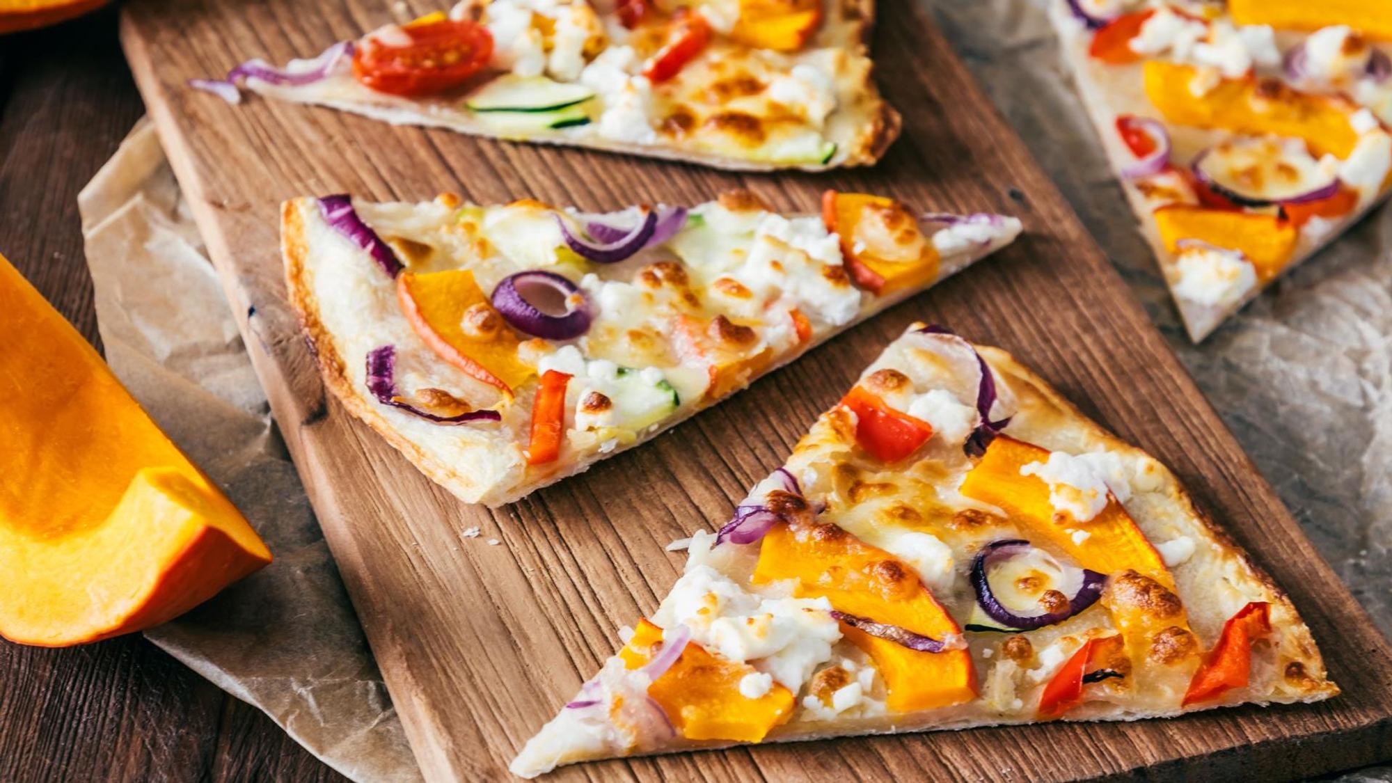 Pizzastücke mit Kürbis liegen auf einem Holzbrett