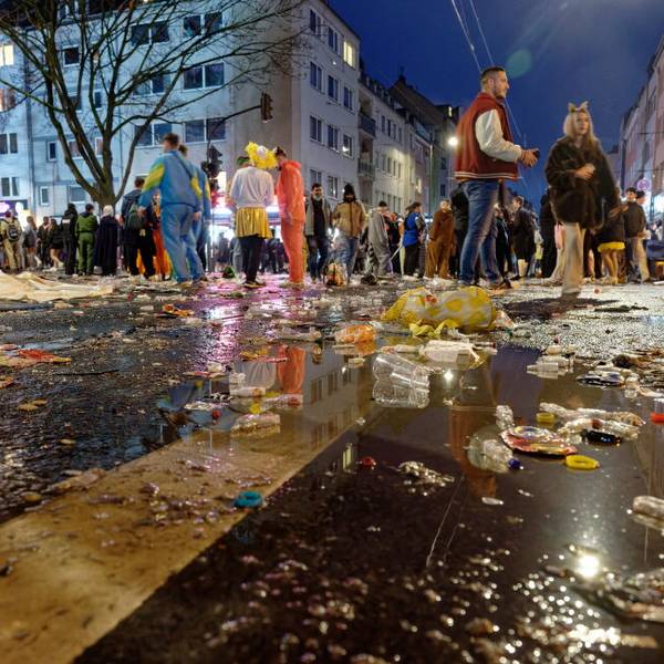 Müll liegt am späten Abend auf der Zülpicher Straße, im Hintergrund stehen kostümierte Menschen in kleinen Gruppen zusammen.