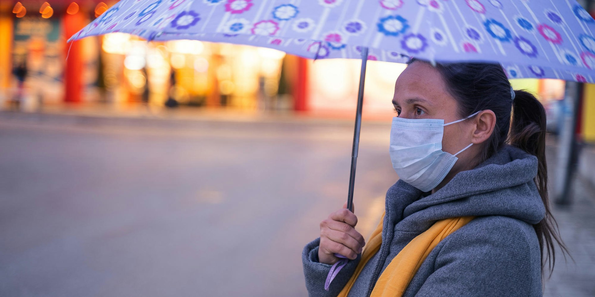 Frau mit Regenschirm und Alltagsmaske