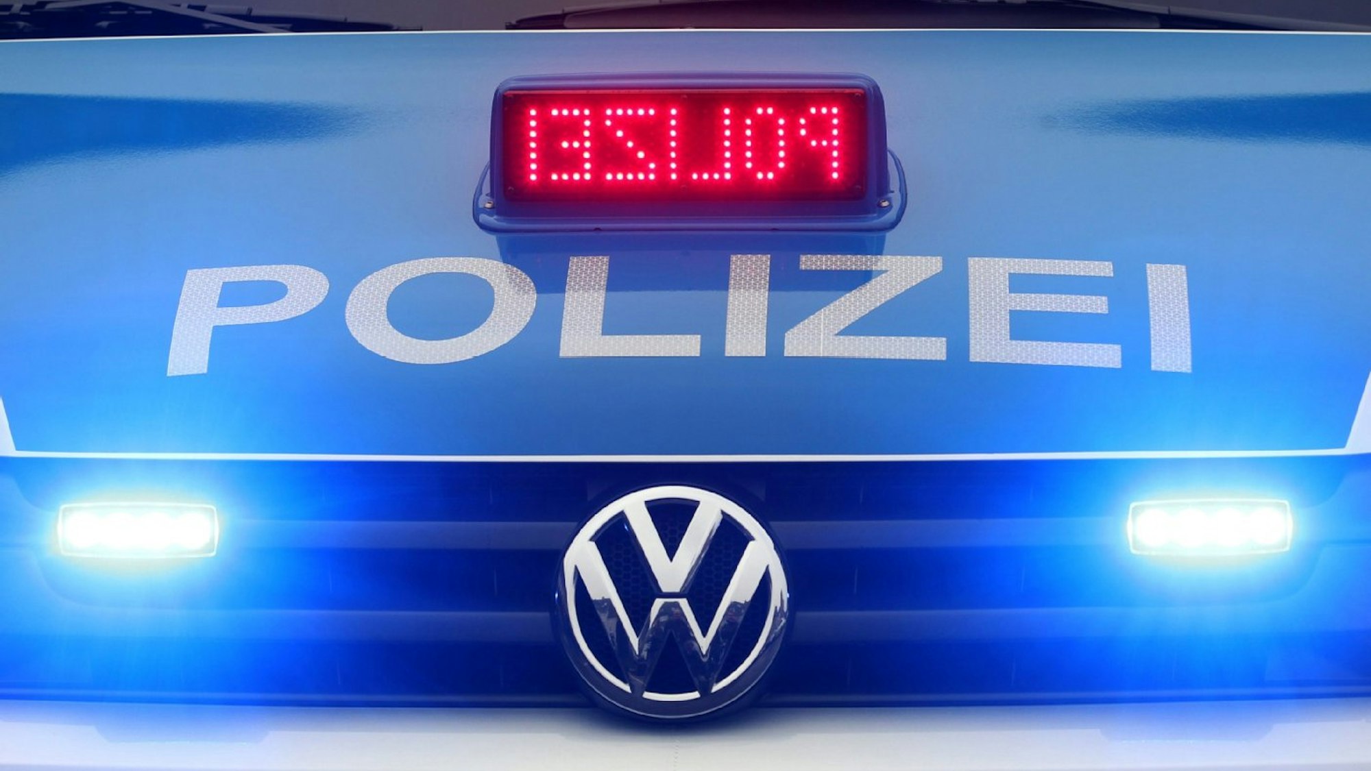 Ein Polizeiauto mit angeschalteten Scheinwerfern und Polizei-Schriftzug ist von vorne zu sehen.