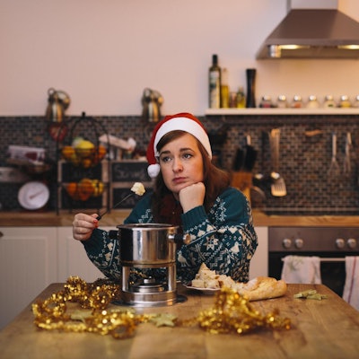 Die Autorin sitzt mit winterlichem Pullover und Nikolaus-Mütze allein am Küchentisch und isst Käse-Fondue.