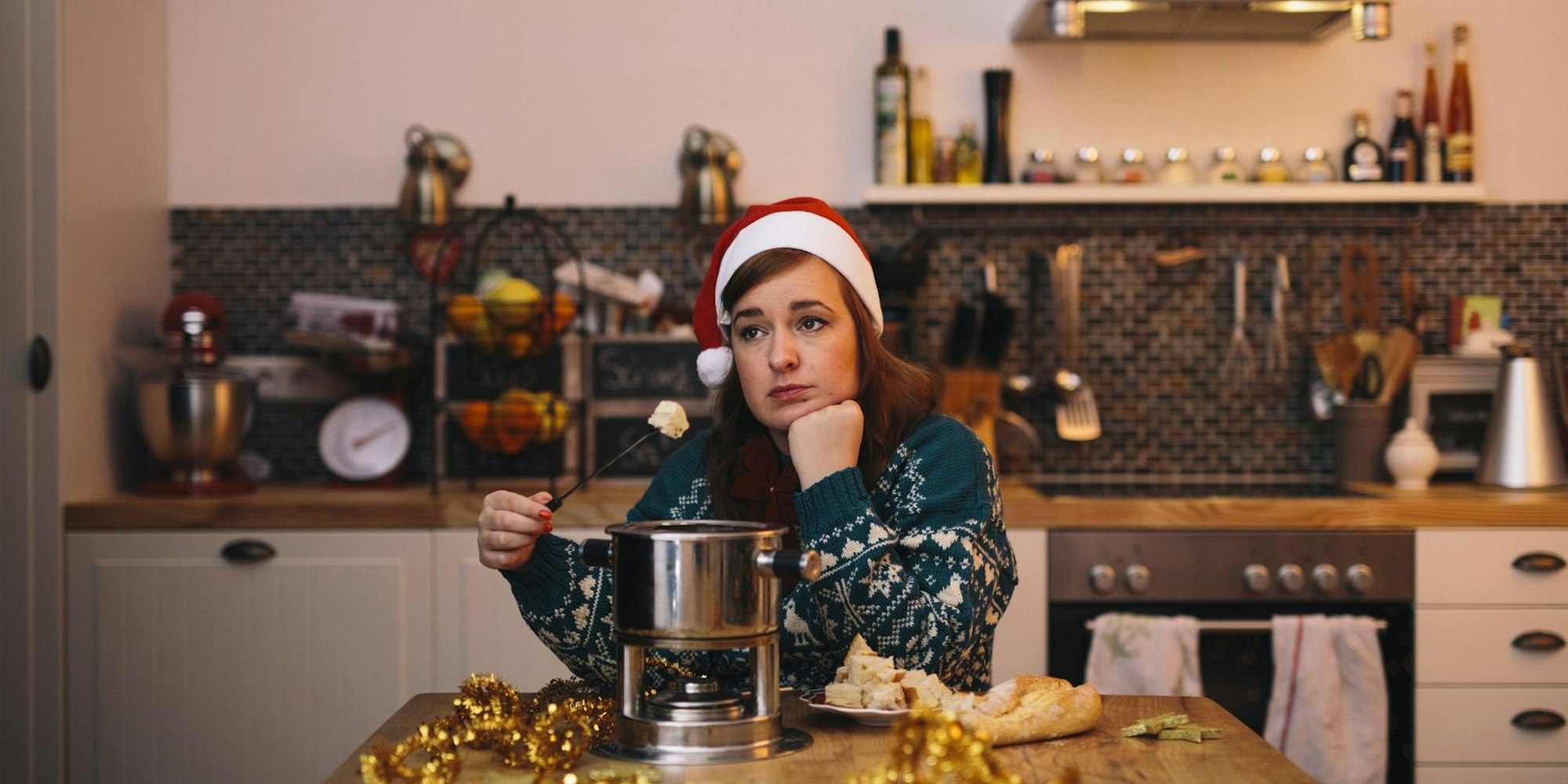 Die Autorin sitzt mit winterlichem Pullover und Nikolaus-Mütze allein am Küchentisch und isst Käse-Fondue.