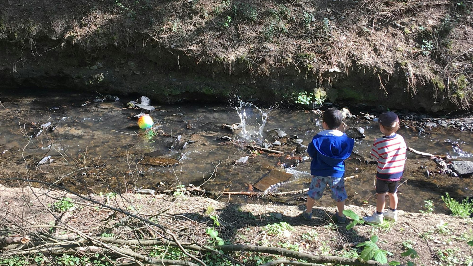 zwei Kinder stehen an einem Bach, in dem ein Ball schwimmt