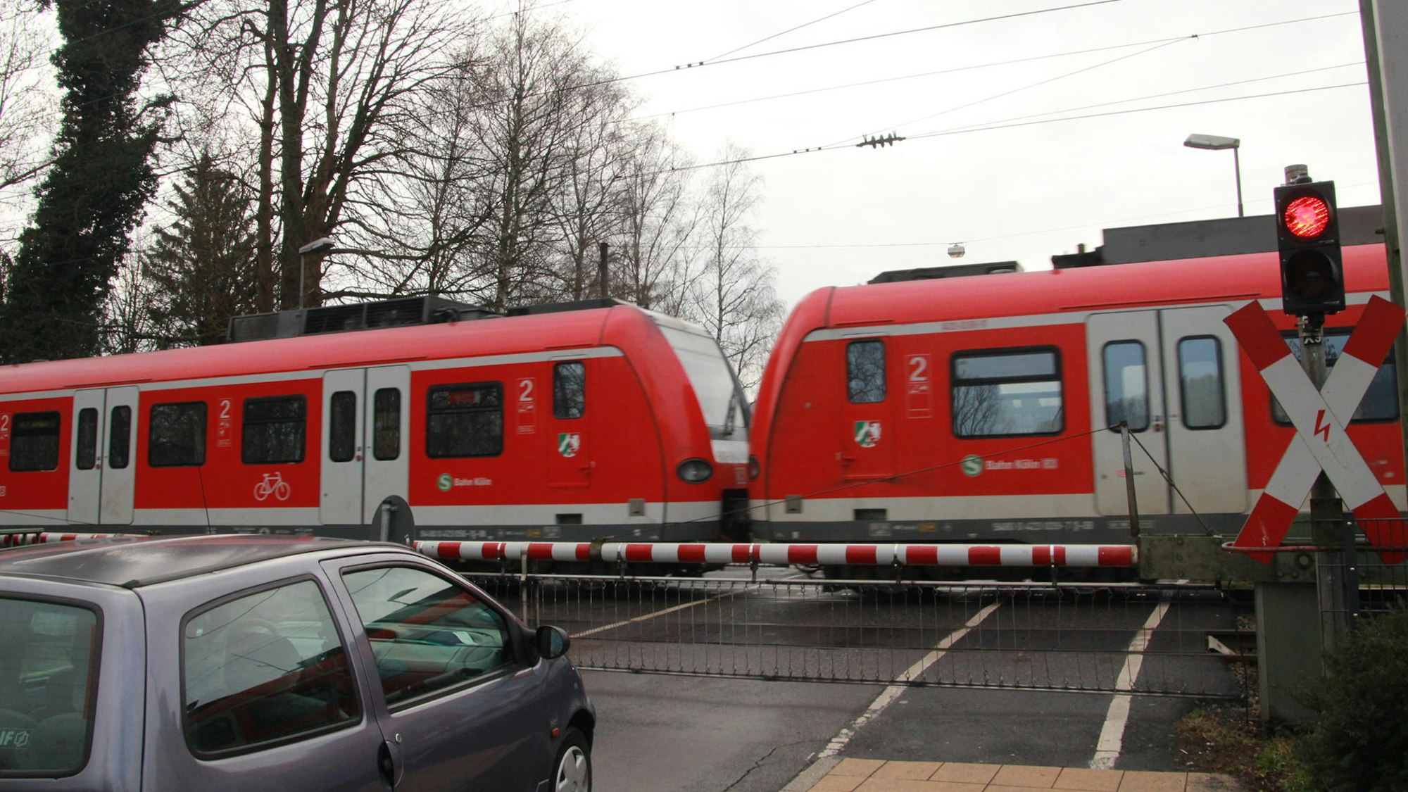 Bahnübergang Brückenstraße in Eitorf, ein Regionalzug fährt durch, während ein Auto vor der Schranke steht.