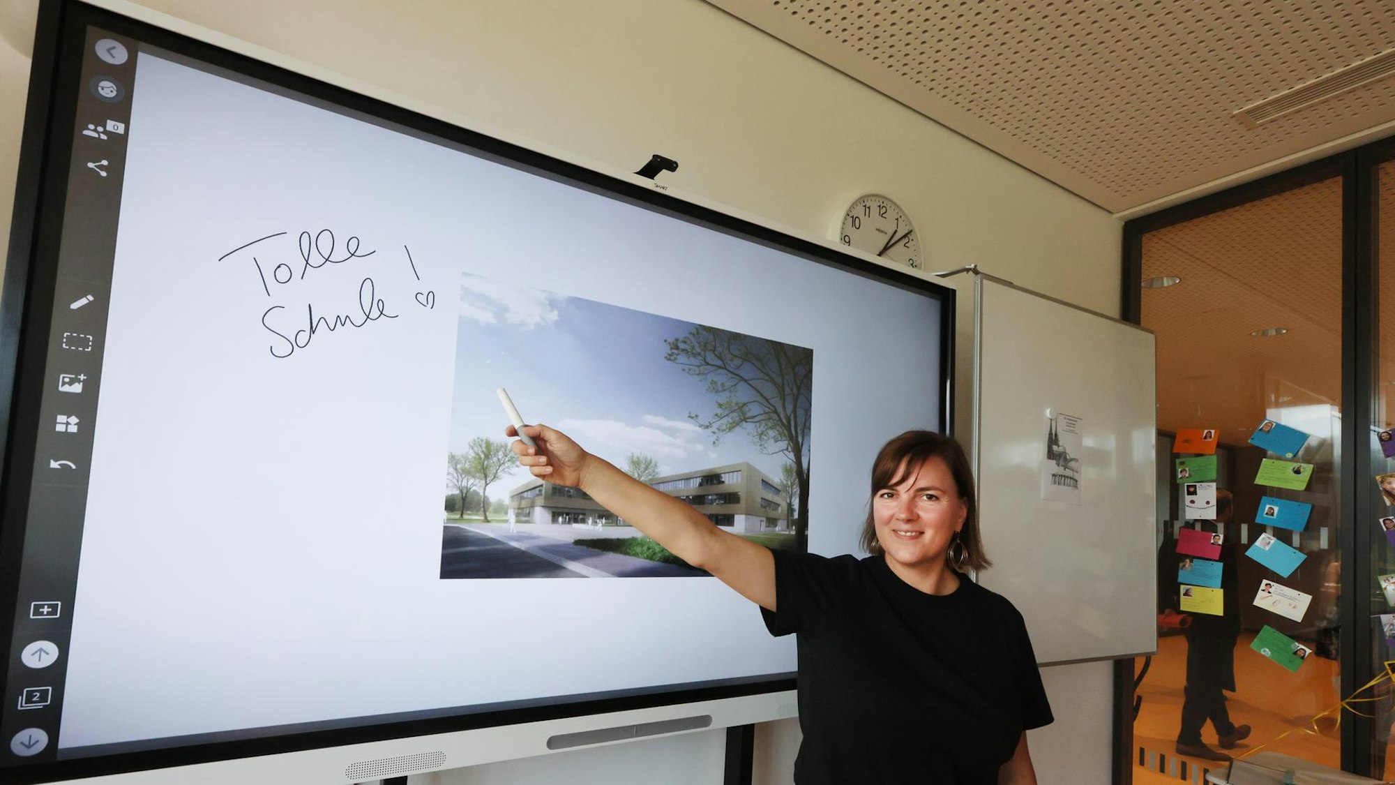 Eine Lehrerin steht in einem Klassenzimmer vor einer digitalen Tafel.