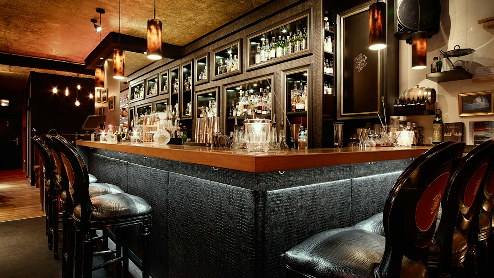 gepolsterte Barstühle stehen an einem in dunkeln Farben gehaltenen Tresen