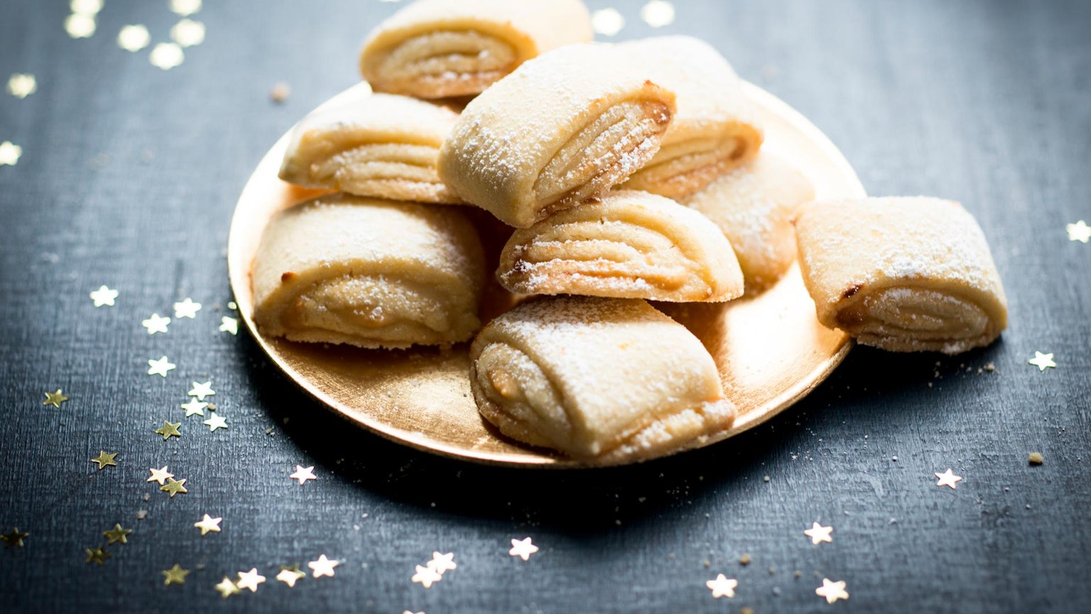 Zuckrige Marzipanballen liegen auf einem Teller angerichtet, rundherum sind goldene Sternchen verteilt