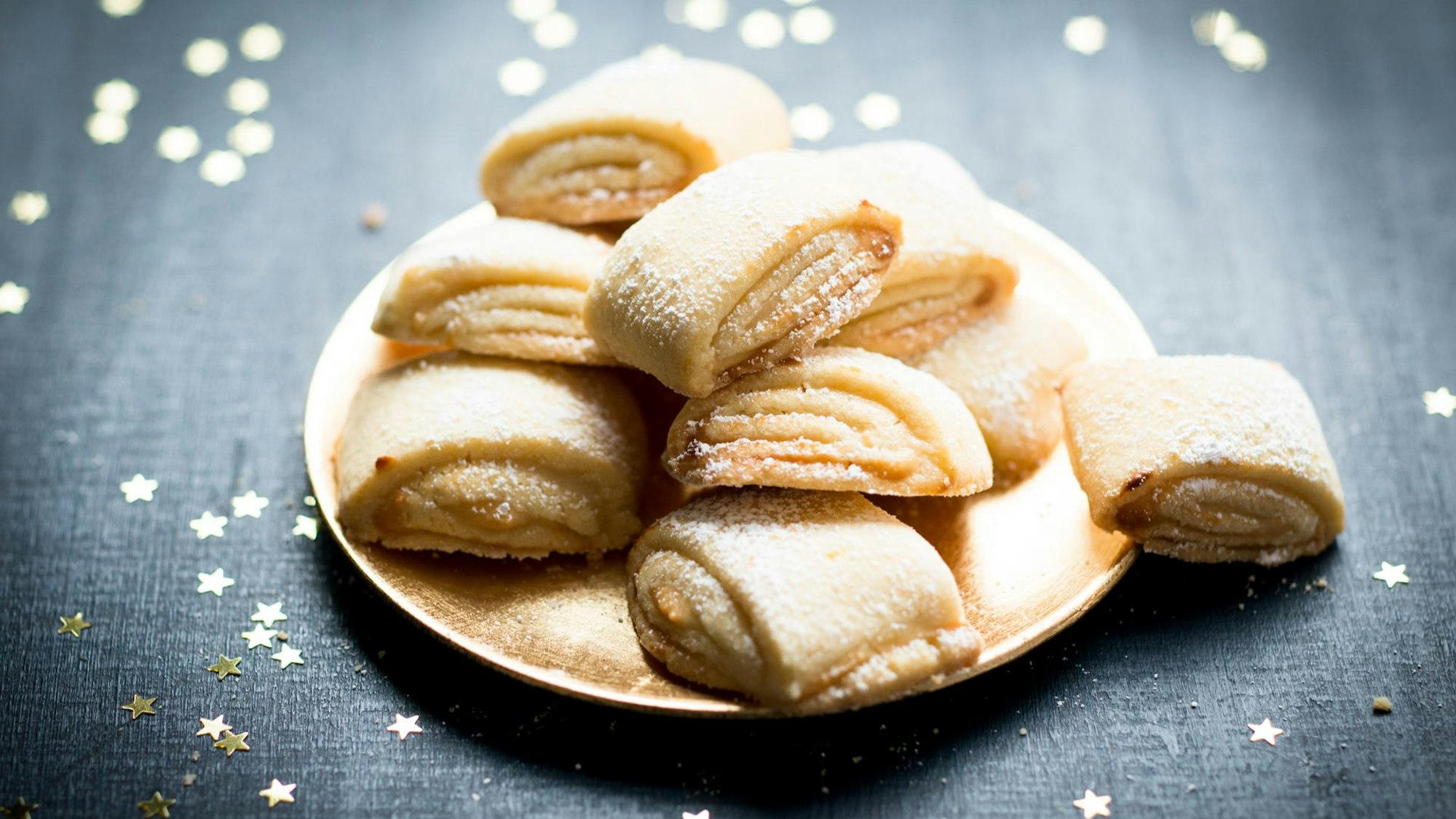 Zuckrige Marzipanballen liegen auf einem Teller angerichtet, rundherum sind goldene Sternchen verteilt