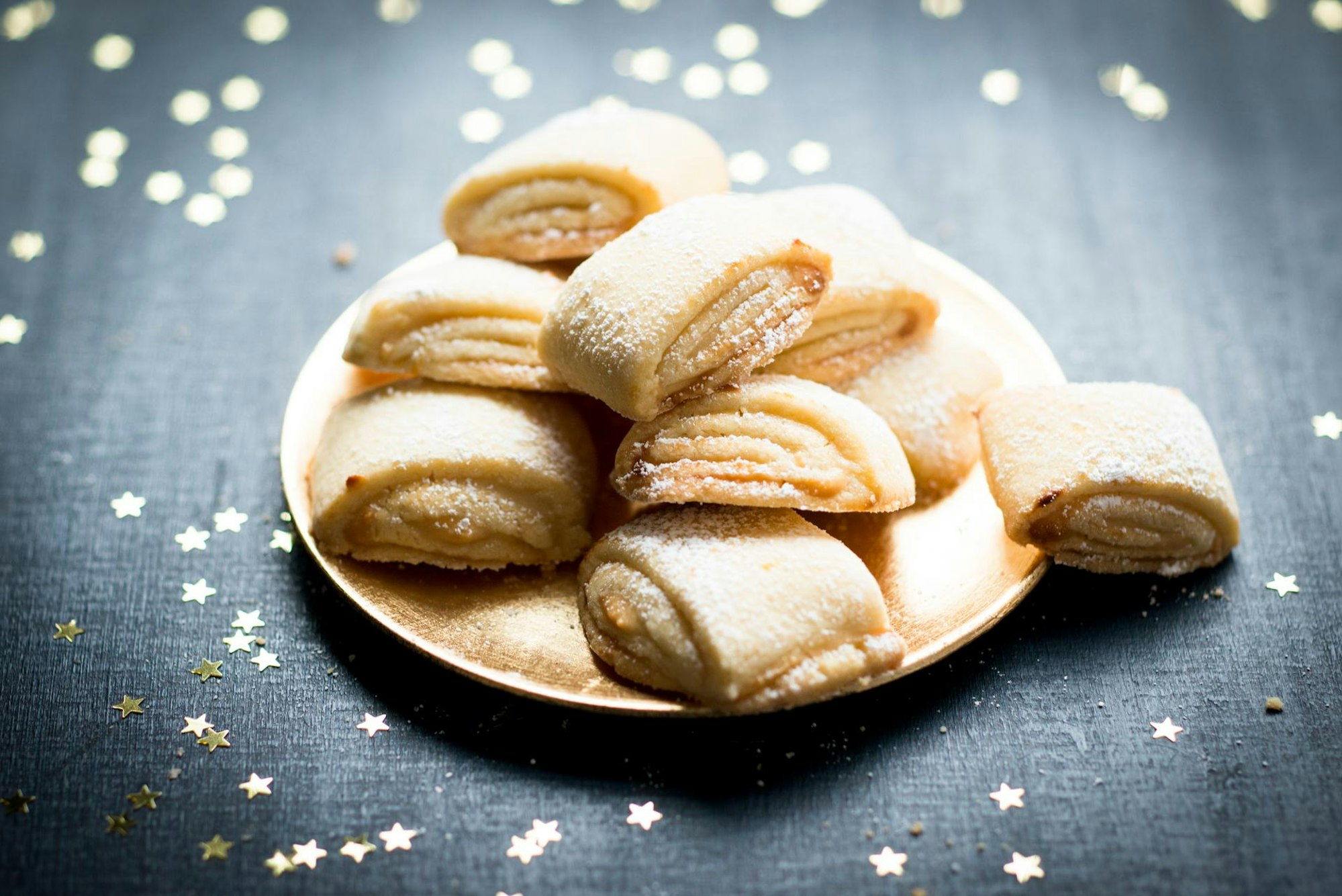 Zuckrige Marzipanballen liegen auf einem Teller angerichtet, rundherum sind goldene Sternchen verteilt