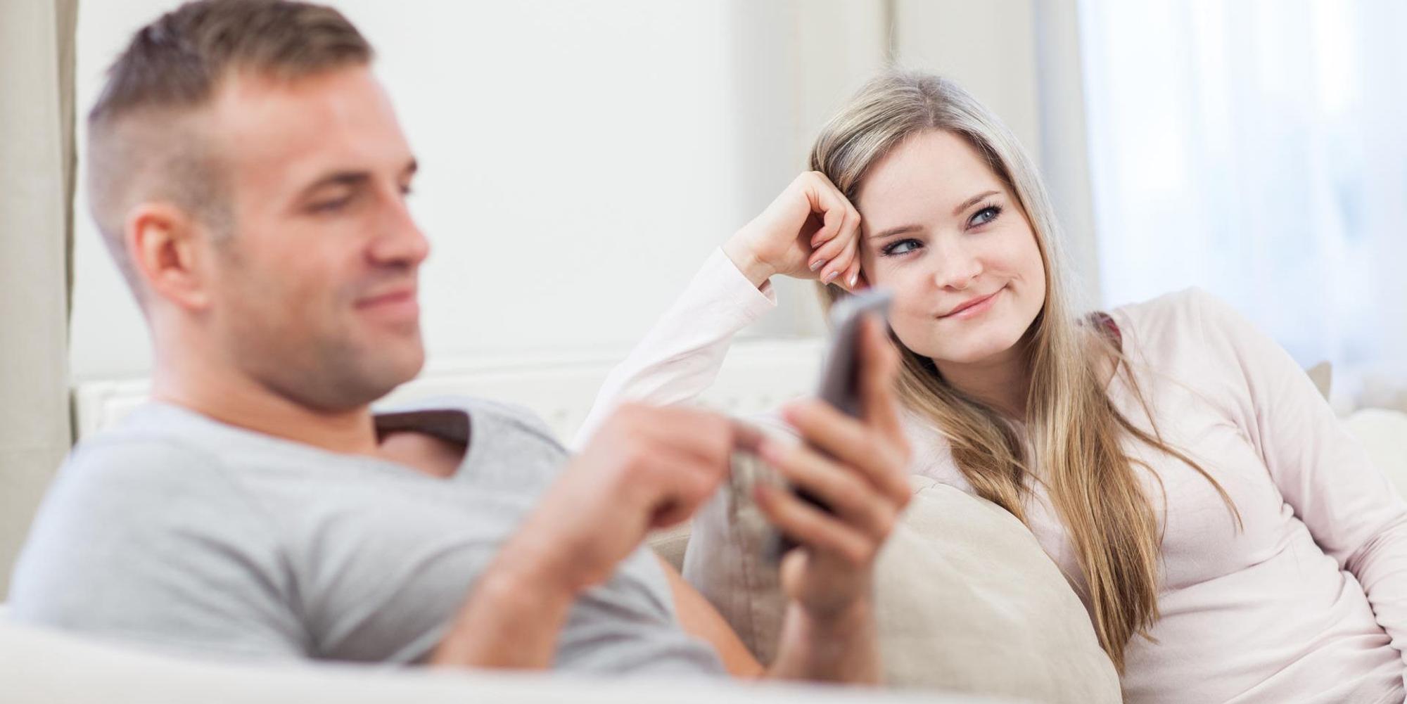 Mann und Frau sitzen auf der Couch: er dattelt, sie ist genervt