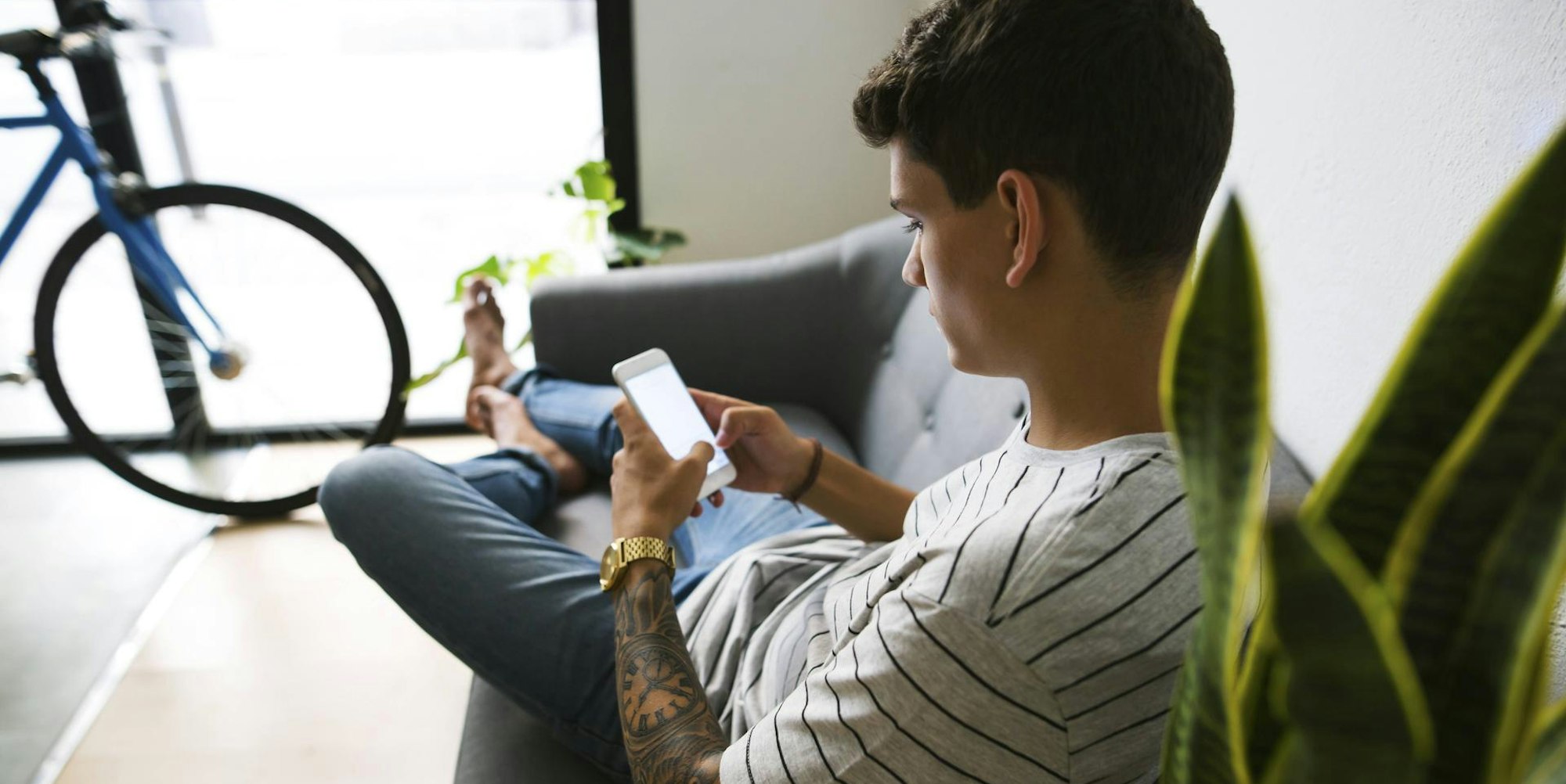 Junge sitzt mit dem Smartphone auf dem Sofa.