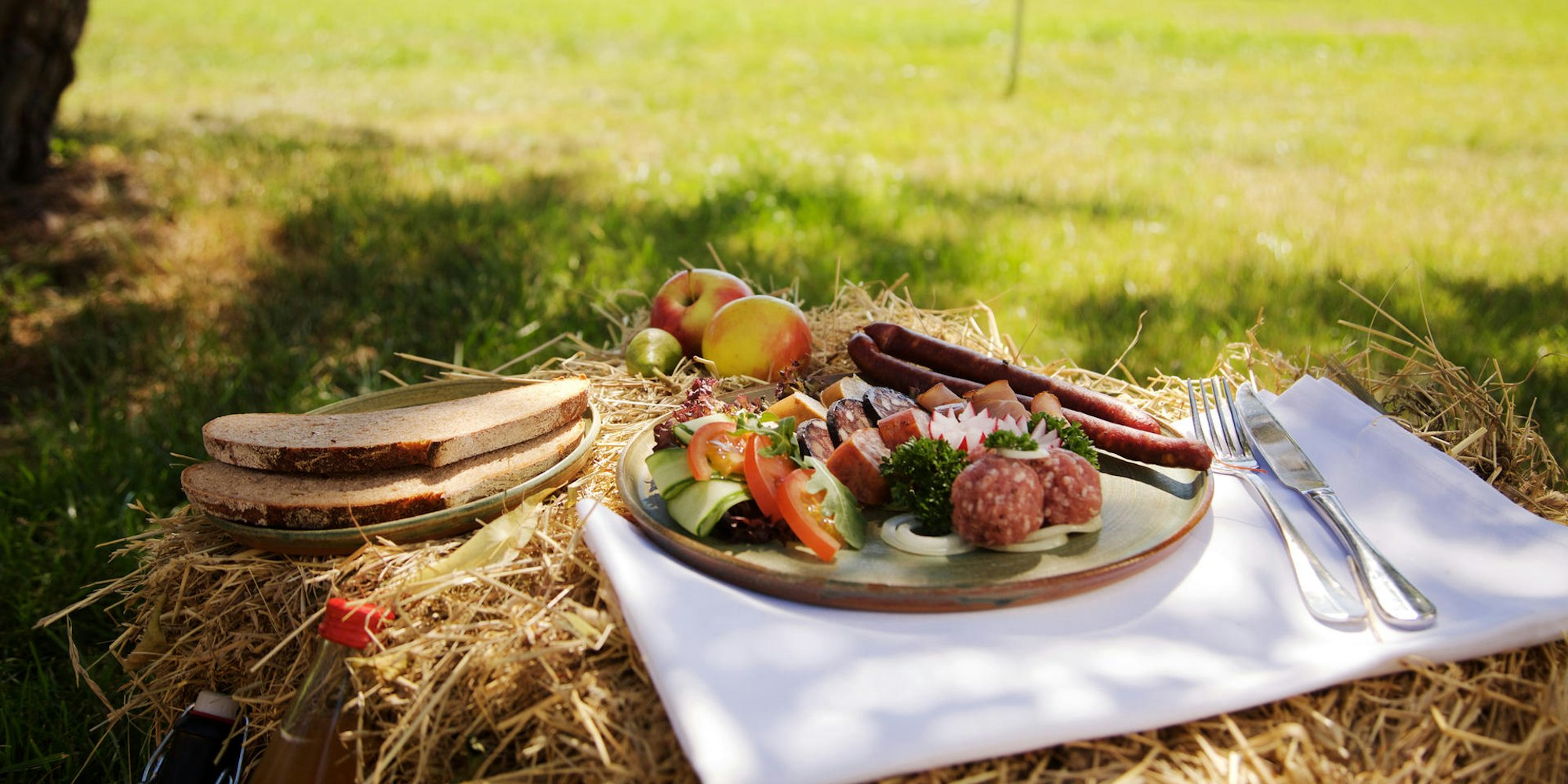Picknickgedeck auf Stroh, dahinter ist eine Wiese zu sehen.