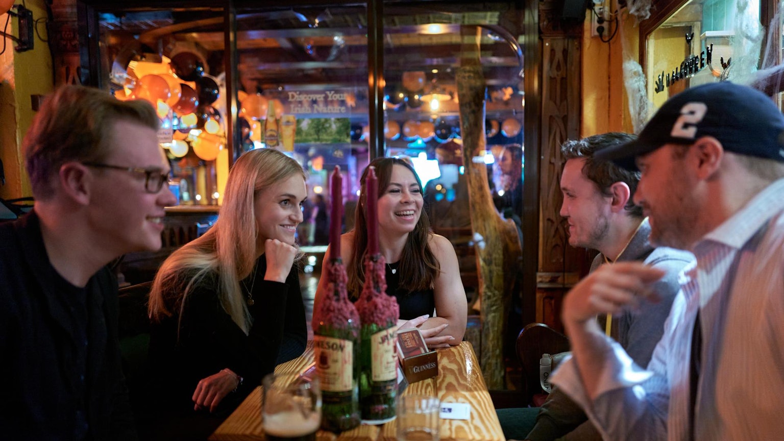 Fünf junge Menschen sitzen in einer Kneipe am Tisch.