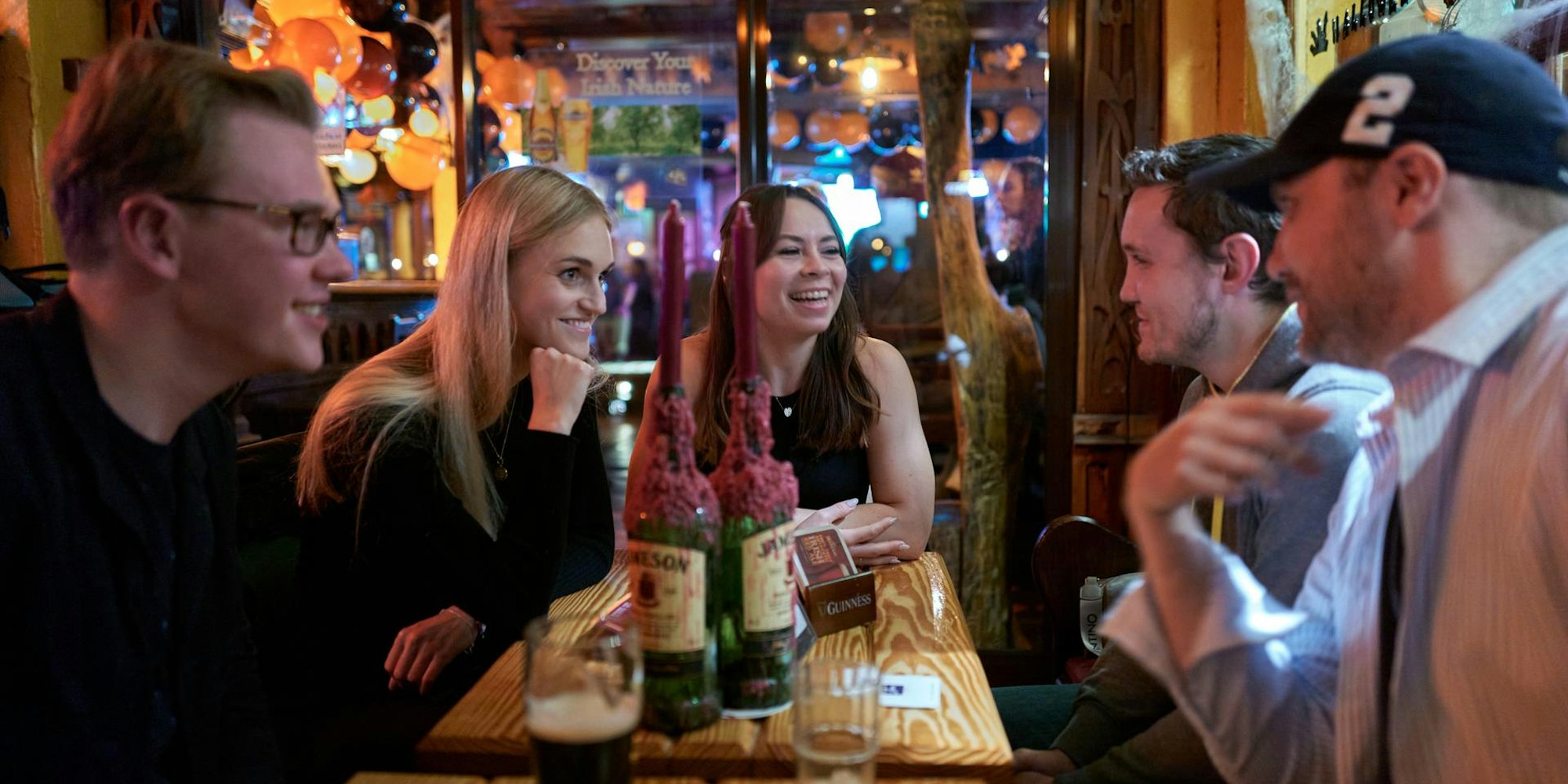 Fünf junge Menschen sitzen in einer Kneipe am Tisch.