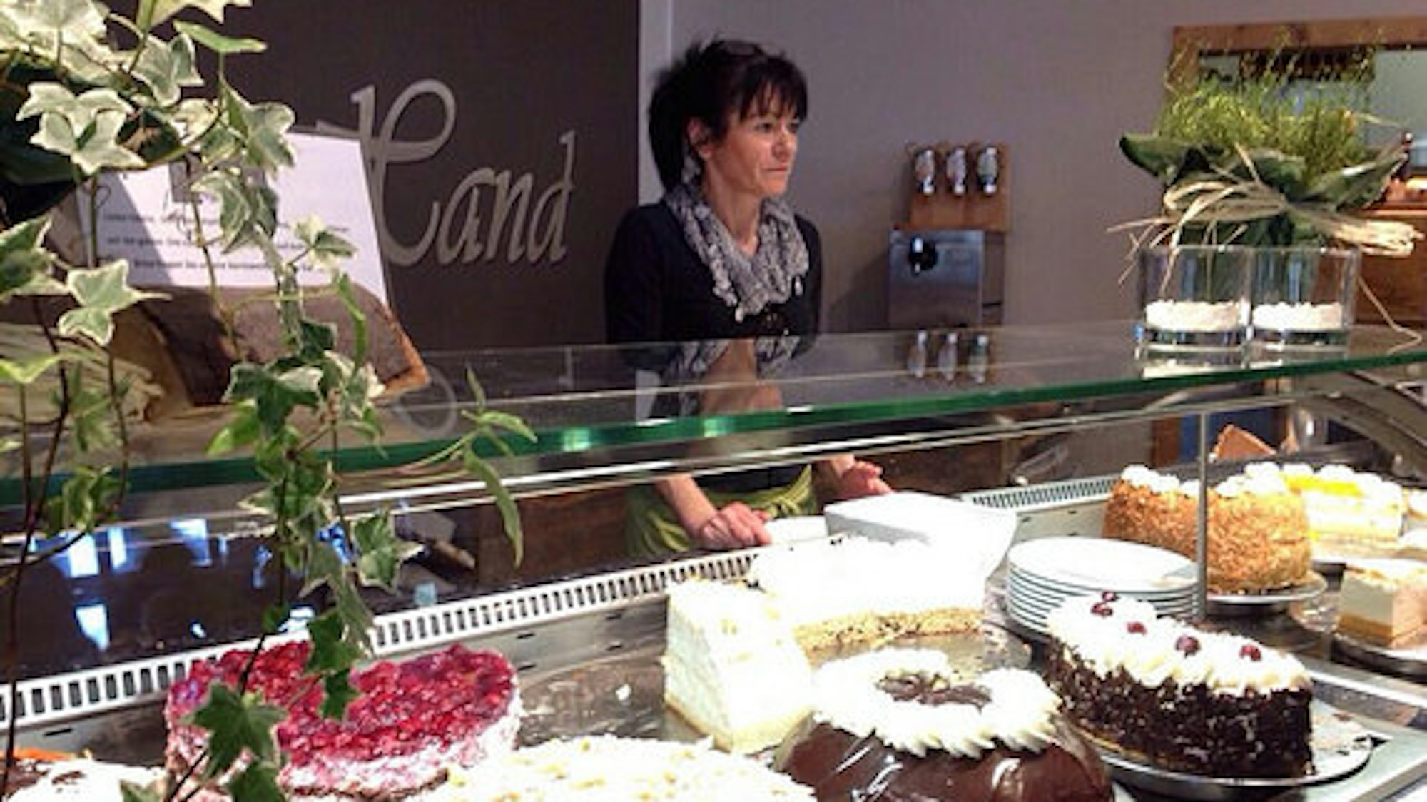 eine Frau steht hinter einer Verkaufstheke mit verschiedenen Torten