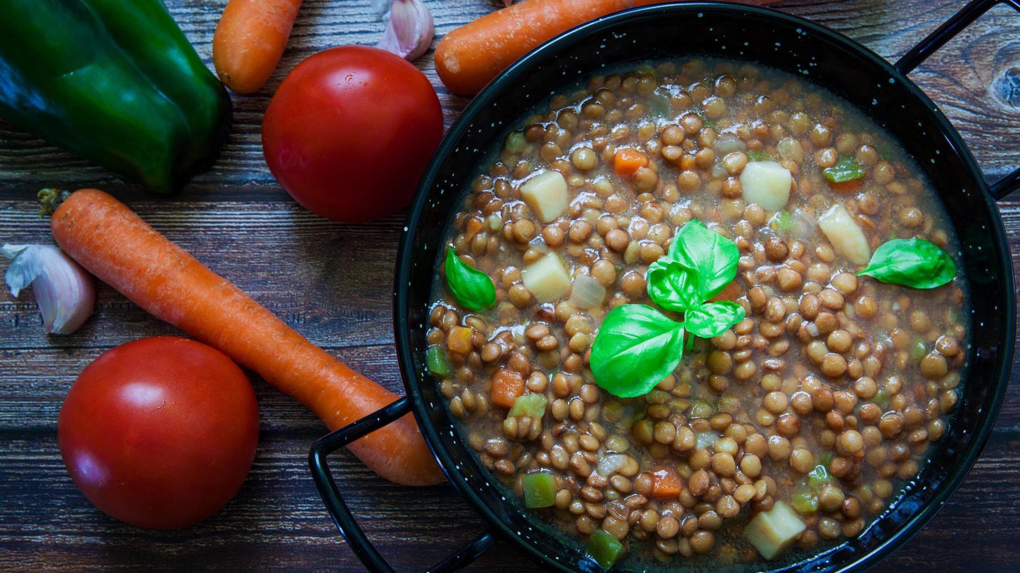 Linseneintopf in einem Topf, daneben Möhren, Tomaten und Paprika