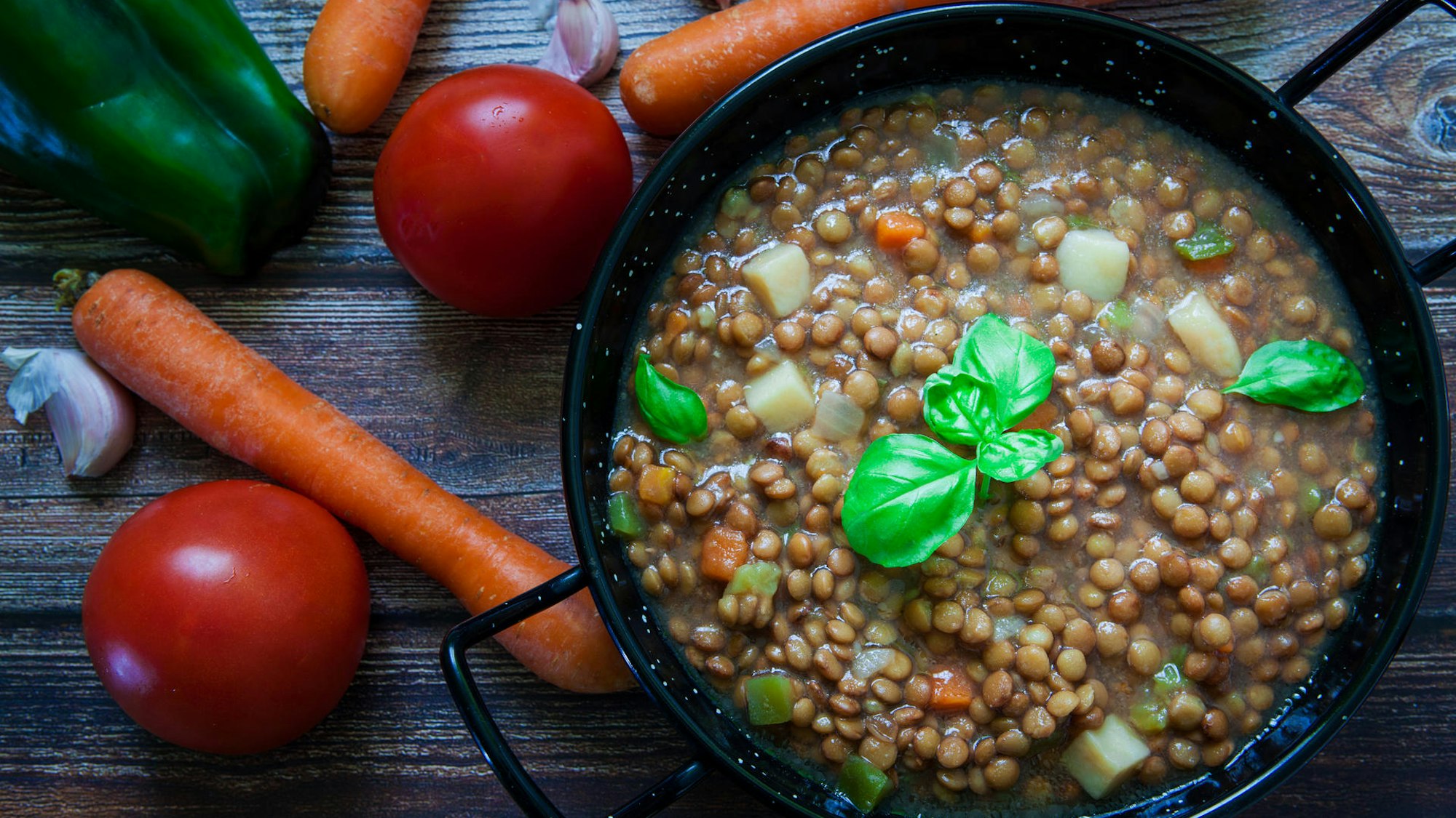 Linseneintopf in einem Topf, daneben Möhren, Tomaten und Paprika