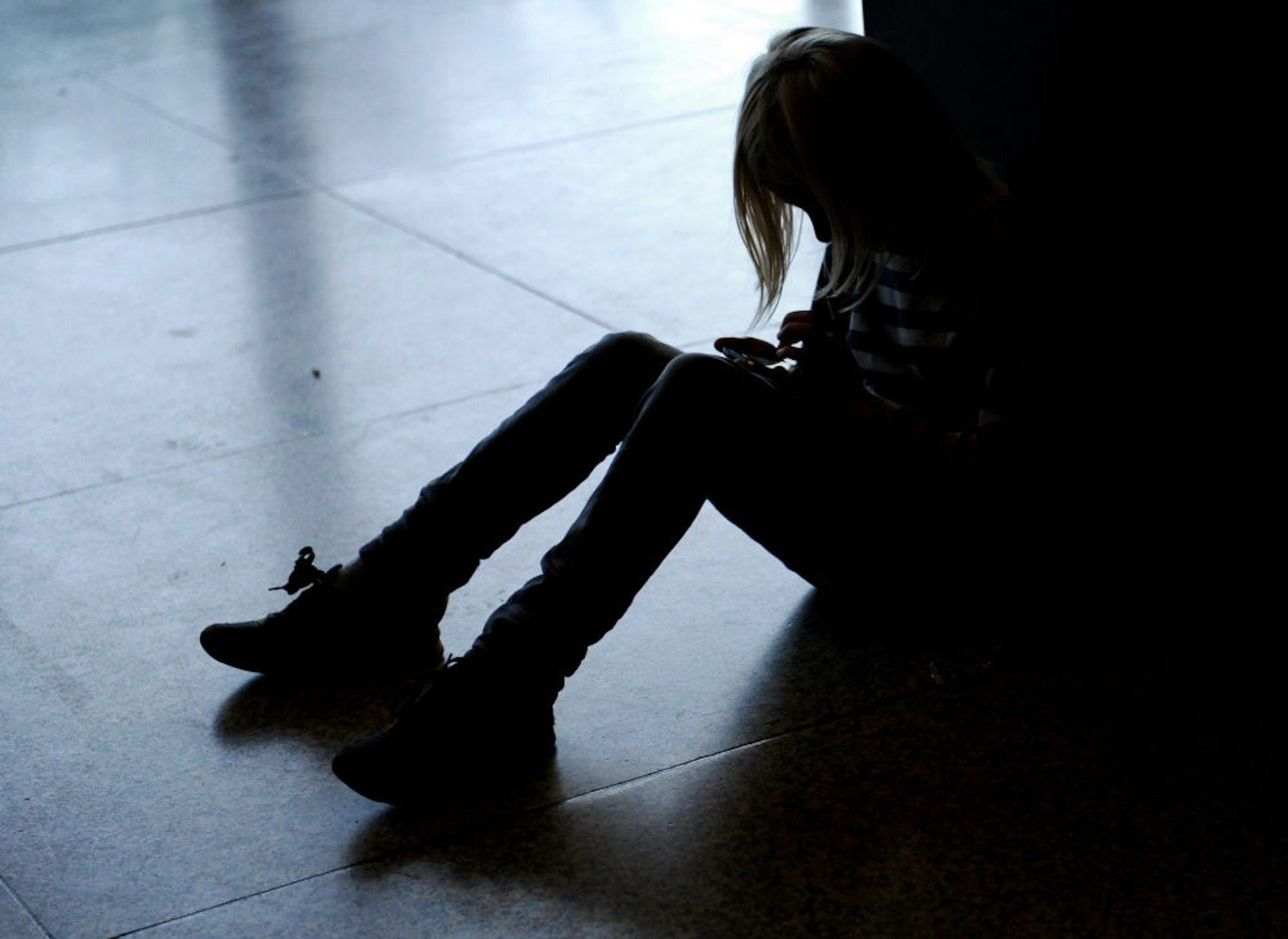 Ein Symbolbild zeigt ein einsames Kind, dass auf dem Fußboden kauert.