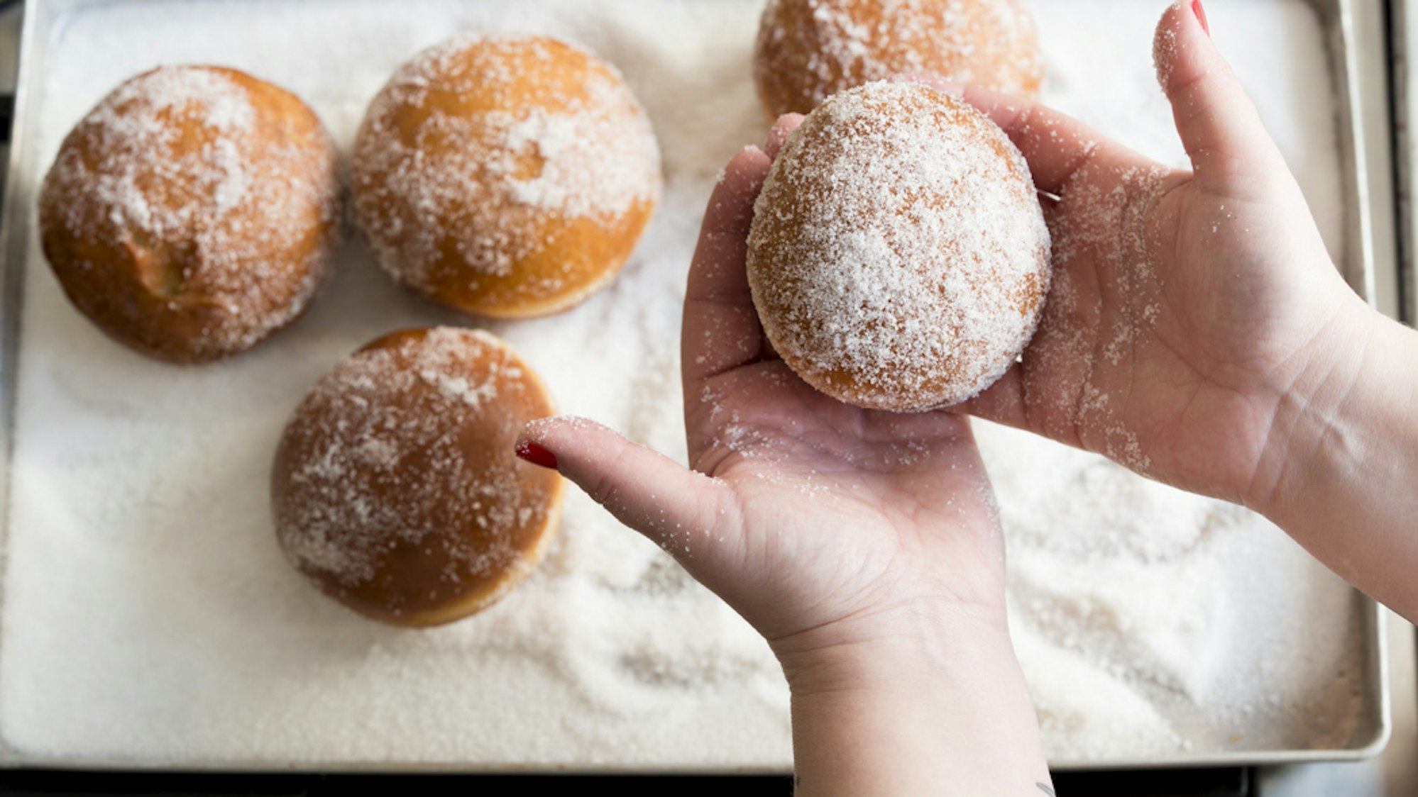 Gebackene Berliner werden in Puderzucker gewälzt.