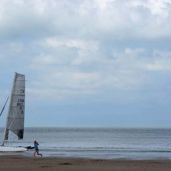 Ein Mädchen läuft am Strand von Cadzand-Bad und ein kleines Segelboot liegt am Strand.