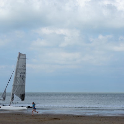 Ein Mädchen läuft am Strand von Cadzand-Bad und ein kleines Segelboot liegt am Strand.