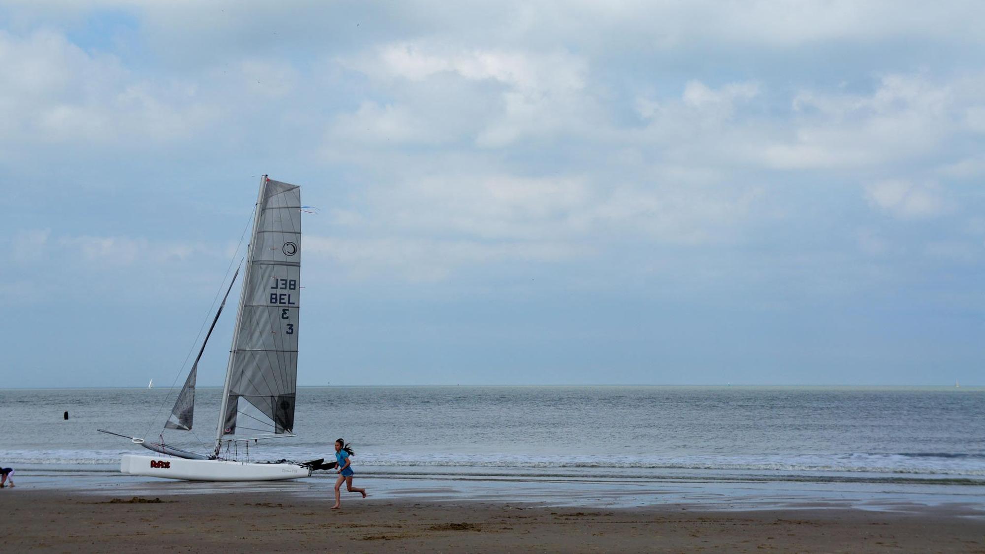 Ein Mädchen läuft am Strand von Cadzand-Bad und ein kleines Segelboot liegt am Strand.