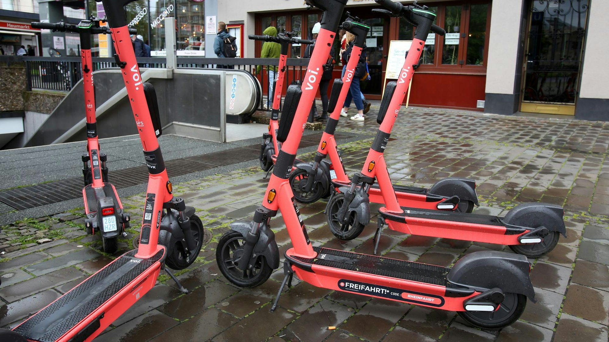 Mehrere E-Scooter des Unternehmens Voi stehen vor einer Rolltreppe zur U-Bahn in der Kölner Innenstadt.