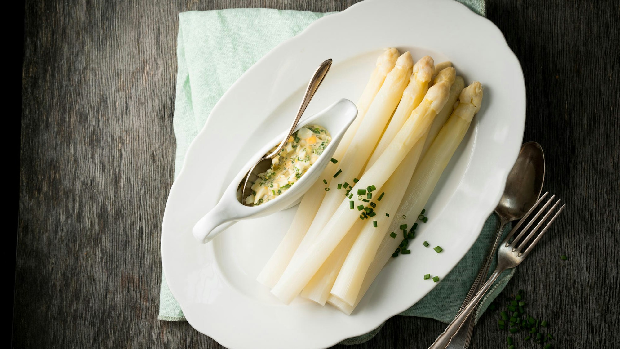 Spargelstangen liegen angerichtet auf einem Teller, Schnittlauch ist sanft darübergestreut, dekorativ.