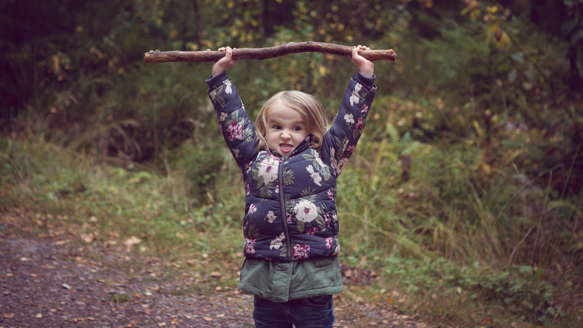 Mädchen hält mit beiden Händen einen Ast in die Luft
