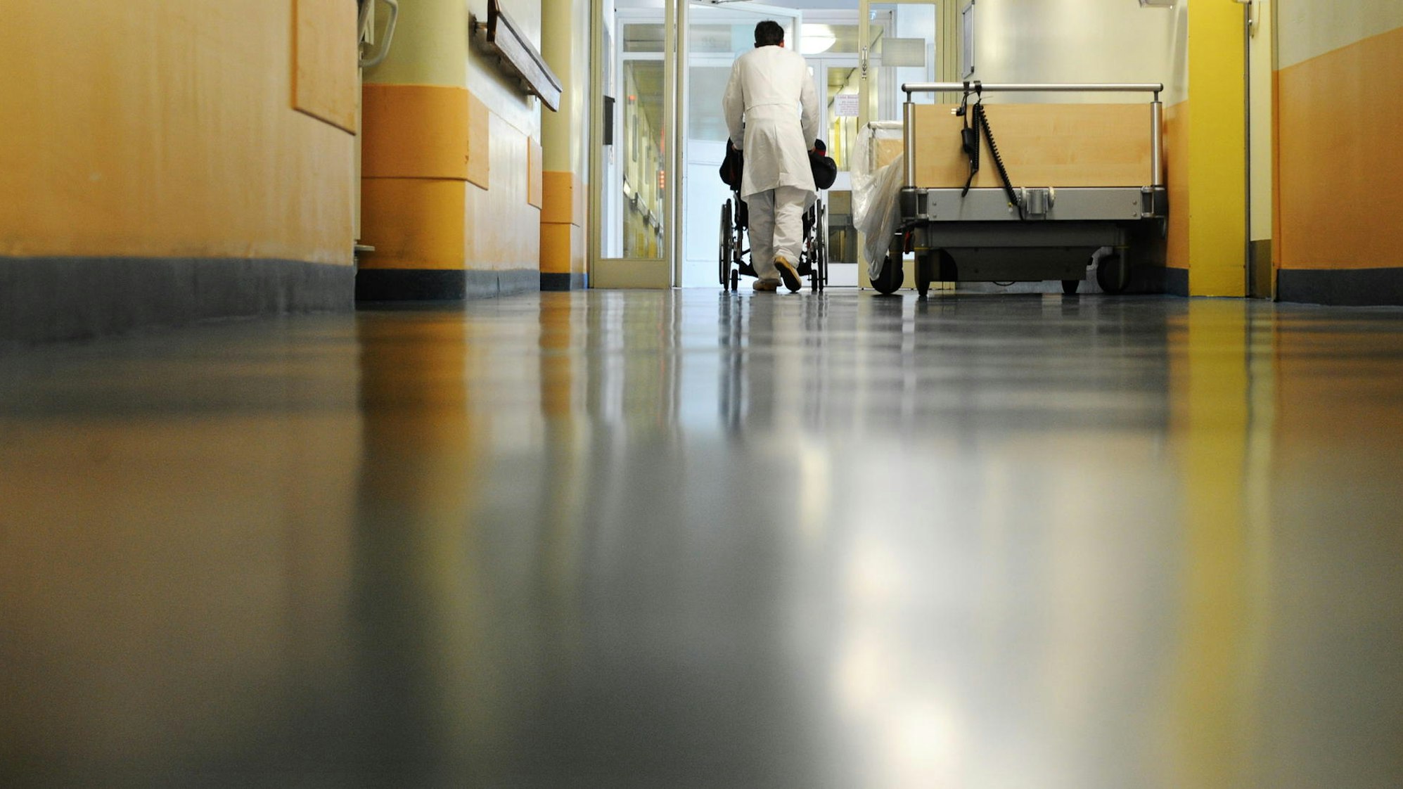Ein Pfleger schiebt eine Patienten im Rollstuhl über den Klinikflur.